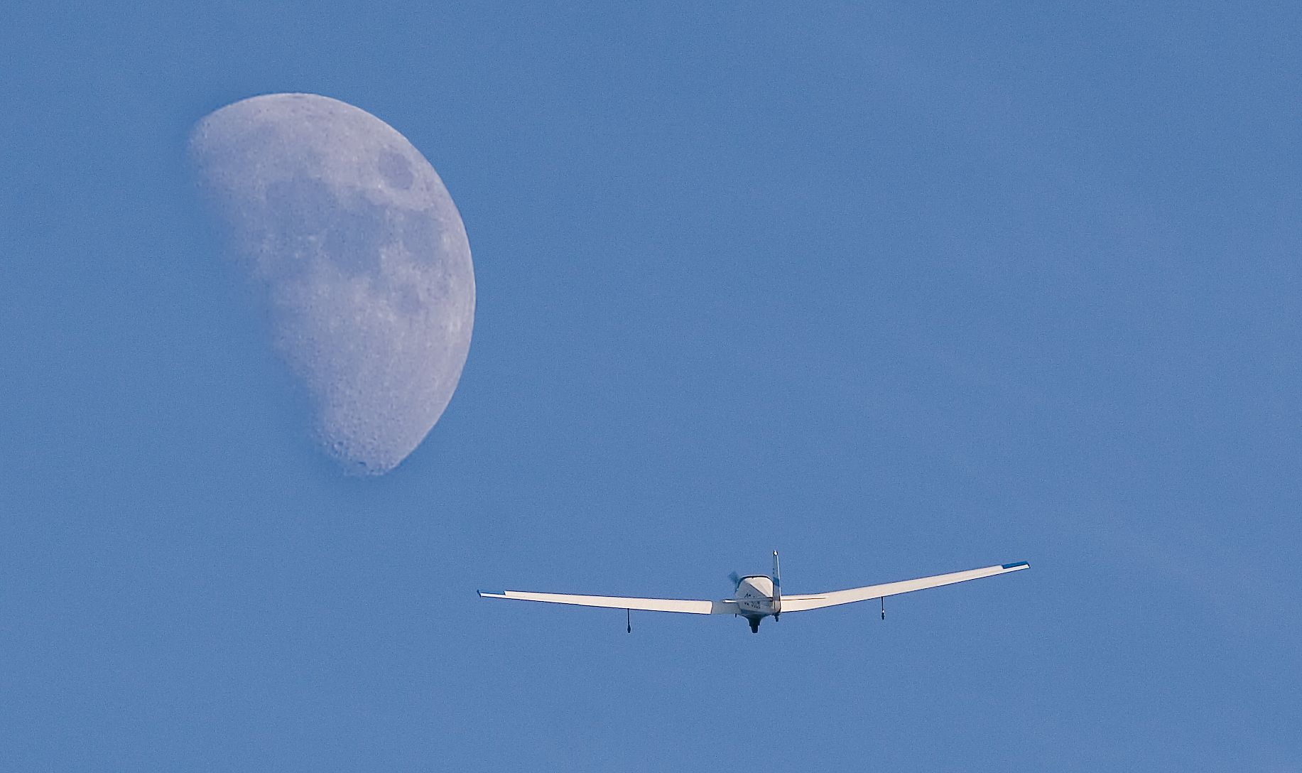 A glider flies in front of a large moon in the blue sky.