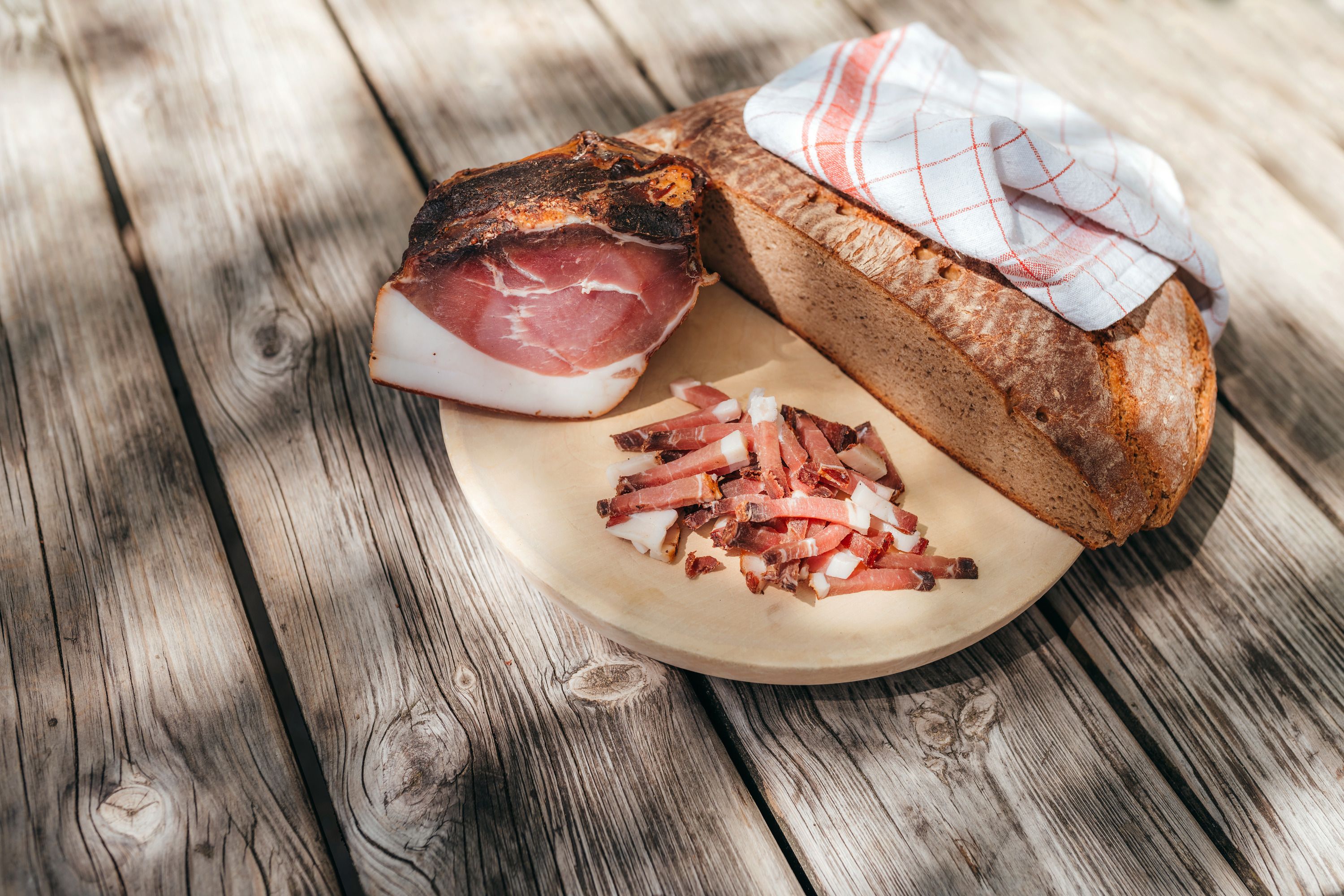 A wooden board with bread, bacon and strips of bacon on a wooden table.