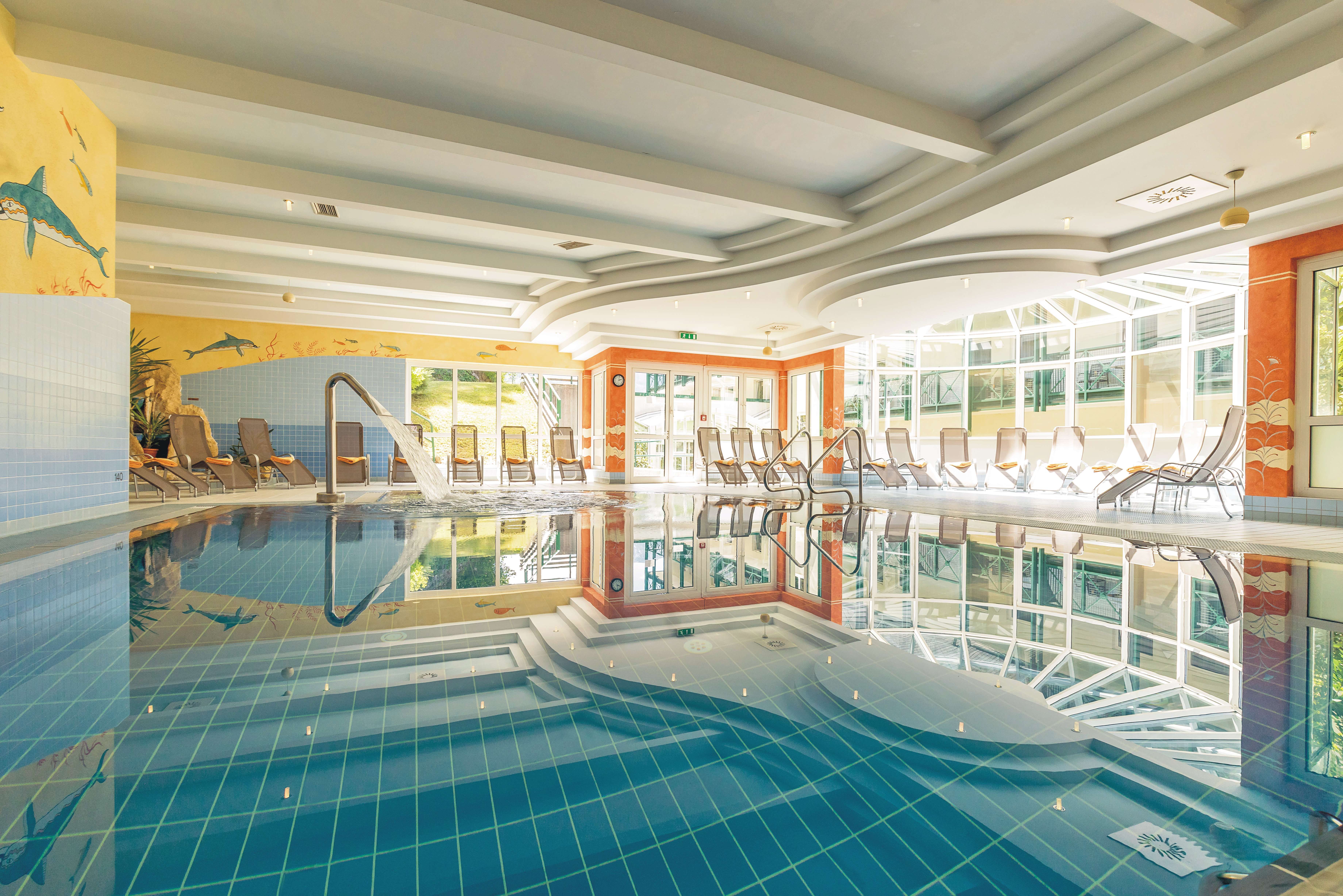 A bright indoor pool with sun loungers and a jet of water in the pool.