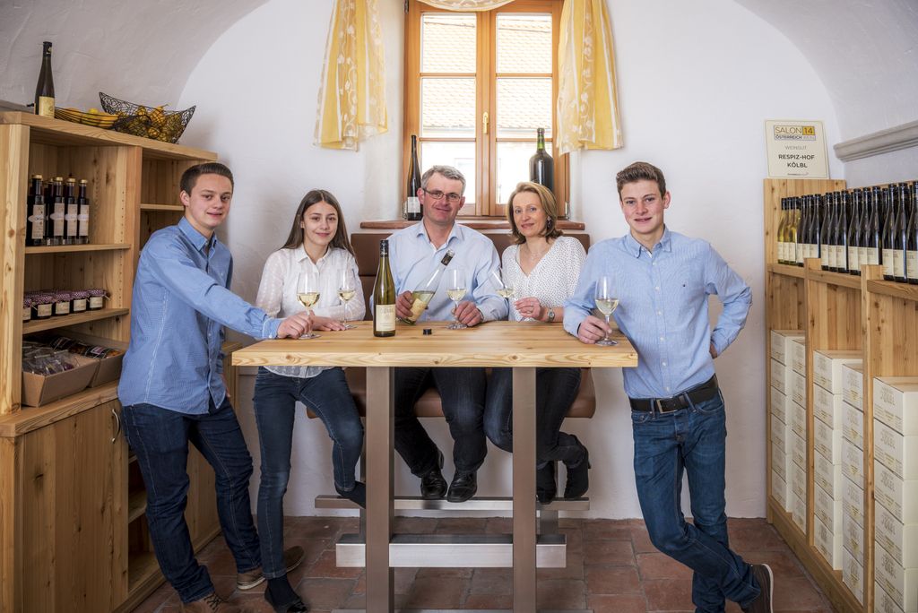 Five people stand around a table in a tasting room with bottles of wine.