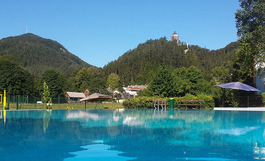 Outdoor pool with a view of wooded hills and a tower in the distance.