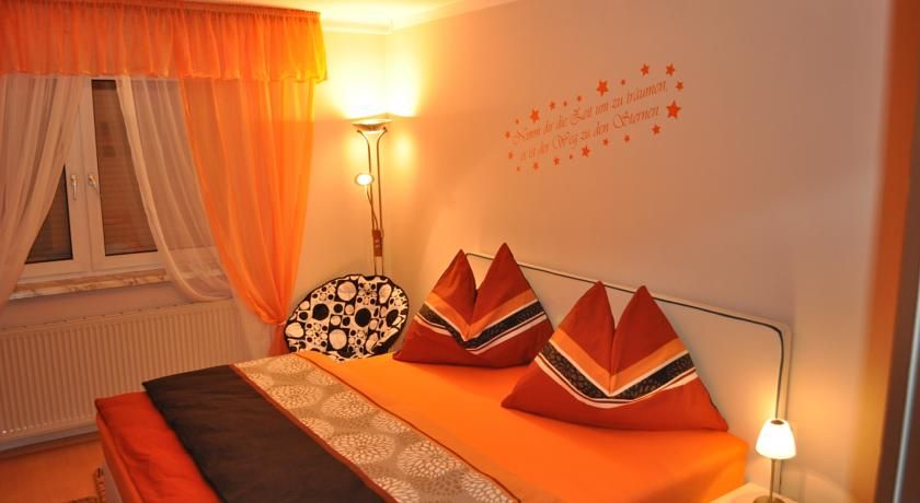 Cozy bedroom with orange bed linen and curtains, decorative cushions and wall tattoo.