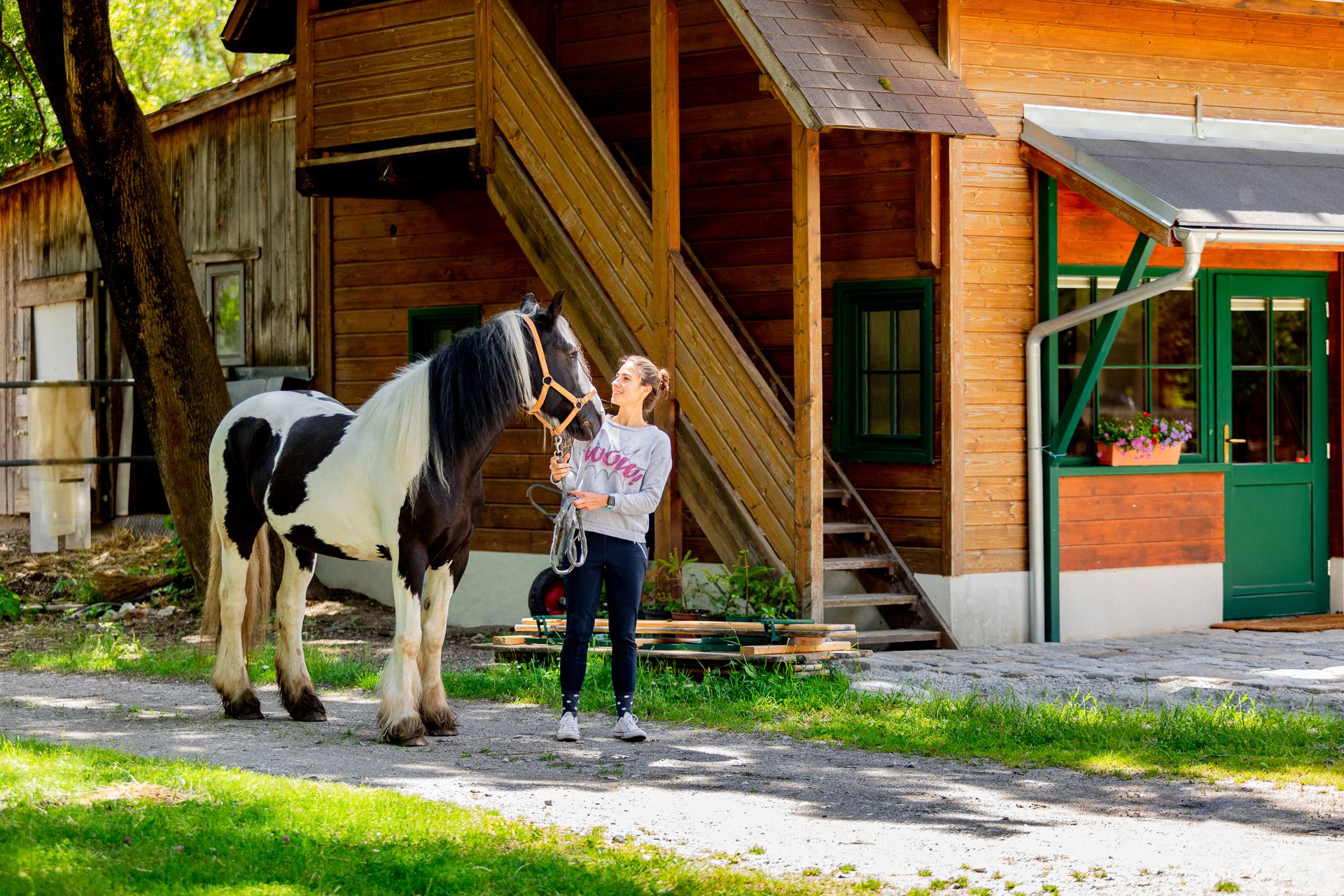 A woman stands next to a black and white horse in front of a wooden building.