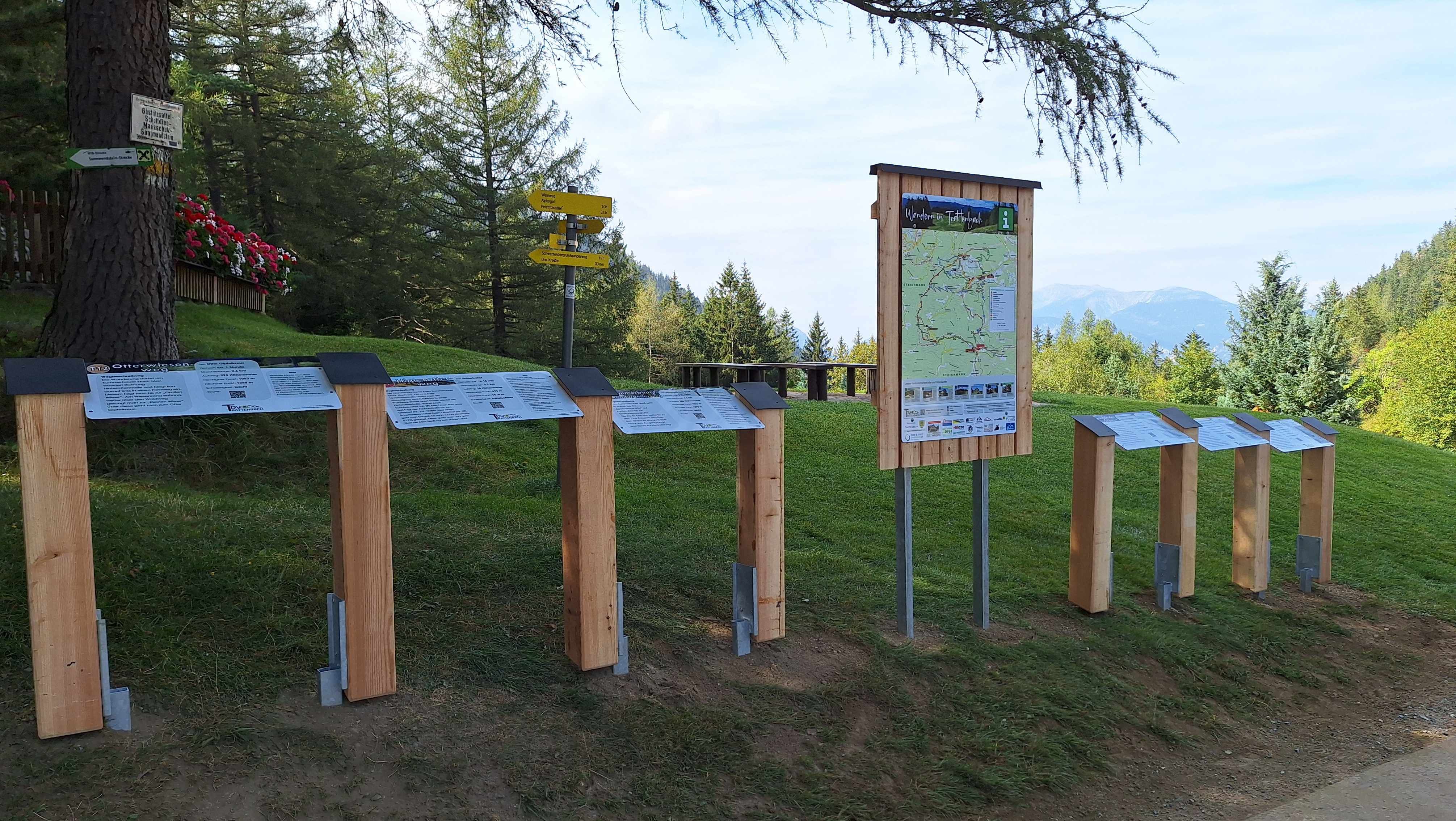 Hiking signposts and information boards in a green, mountainous landscape.