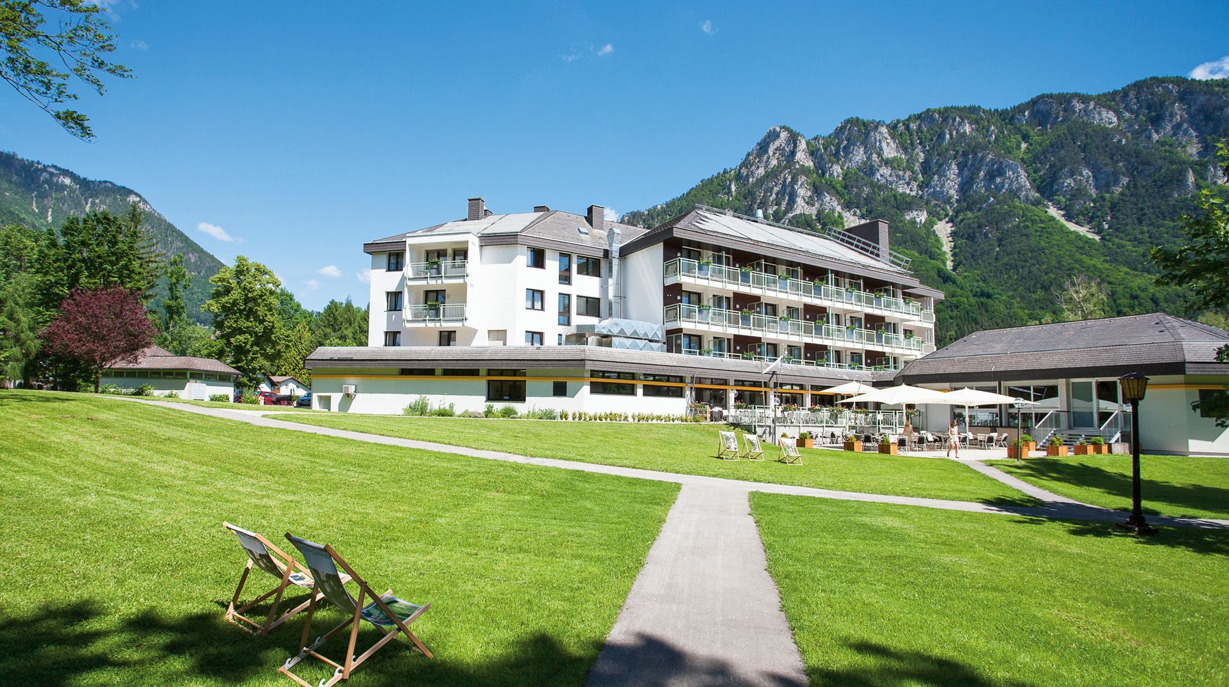Parkhotel Hirschwang against a mountain backdrop with a green lawn and sun loungers.