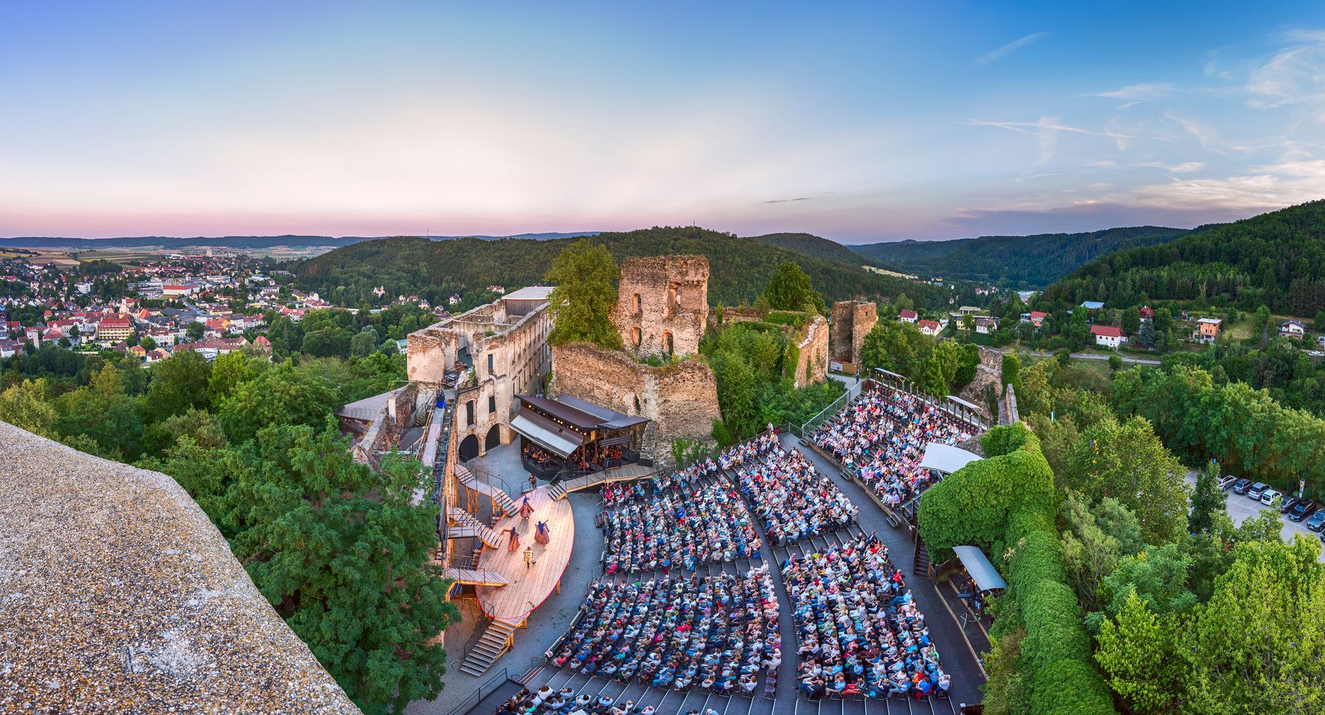 Panoramic view of the opera performance in the Gars castle ruins with audience and surrounding landscape.