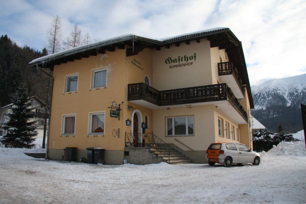 A yellow building with the inscription 'Gasthof Sonnenhof' in the snow, surrounded by mountains.