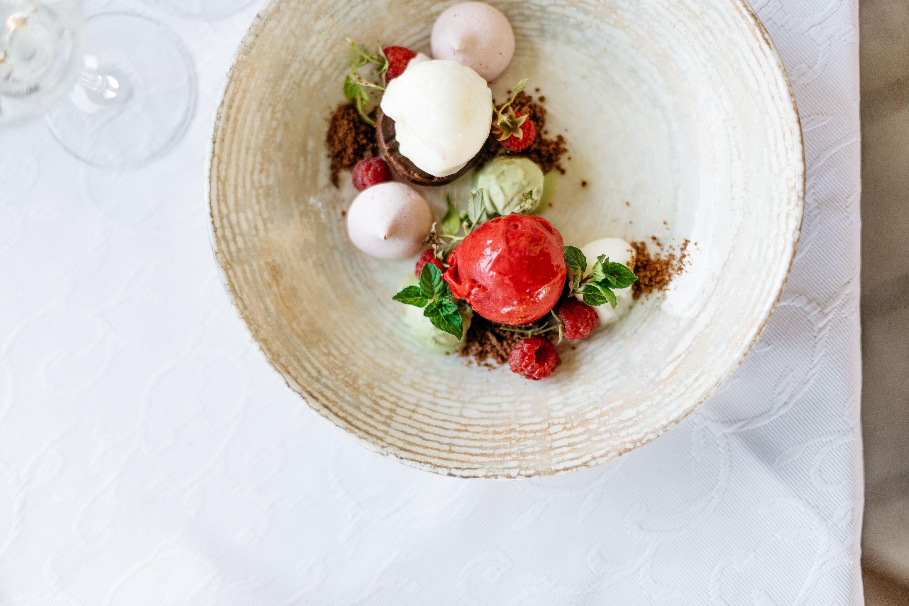 A dessert with various scoops of ice cream, raspberries and mint leaves on a plate.