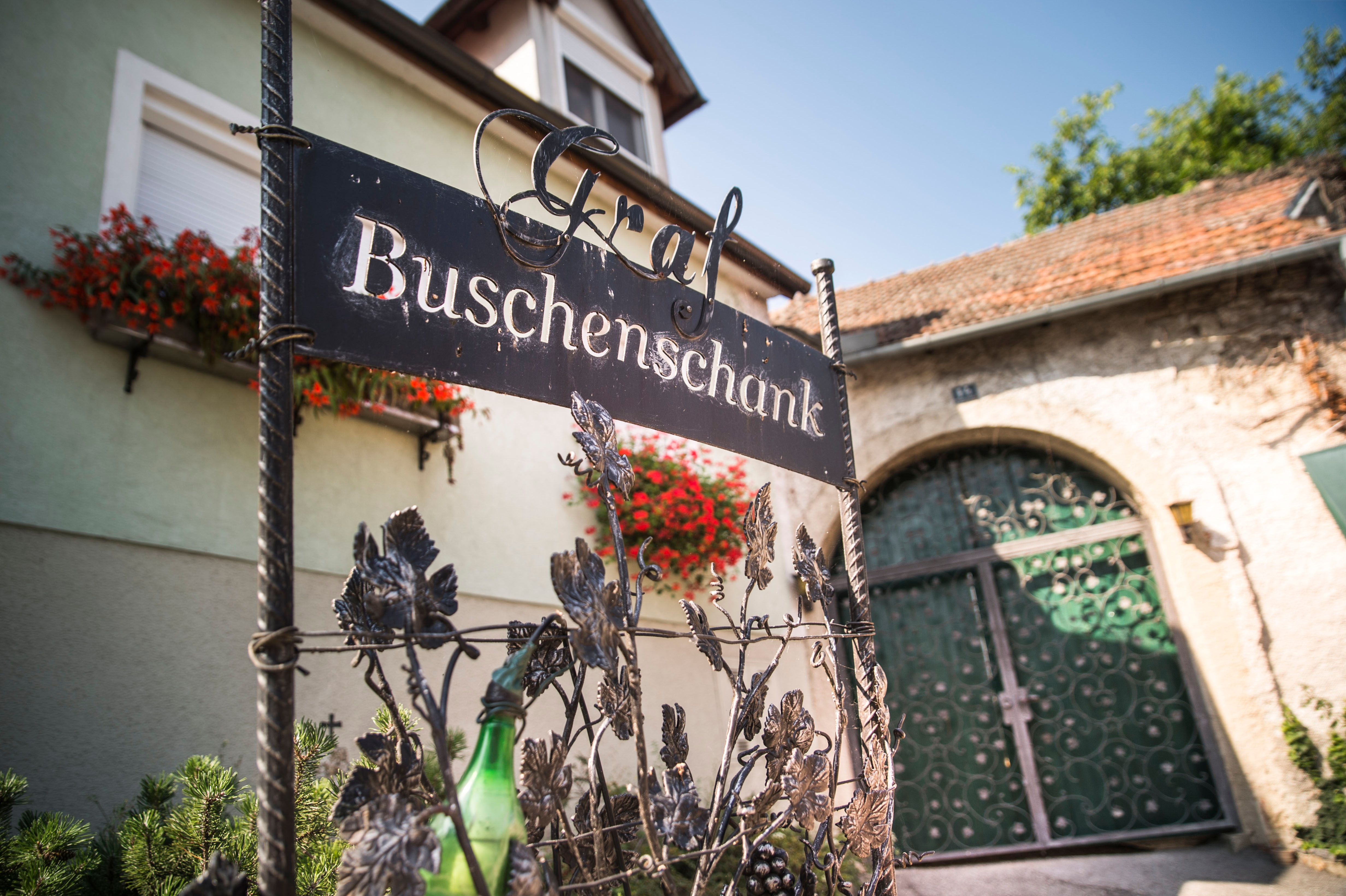Entrance sign of a Buschenschank (typical tavern) with flowers and gate in the background.