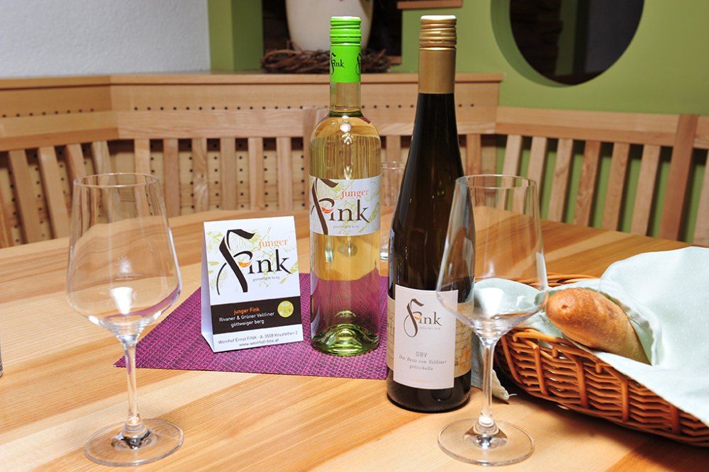 Two bottles of wine and glasses on a wooden table with a bread basket.