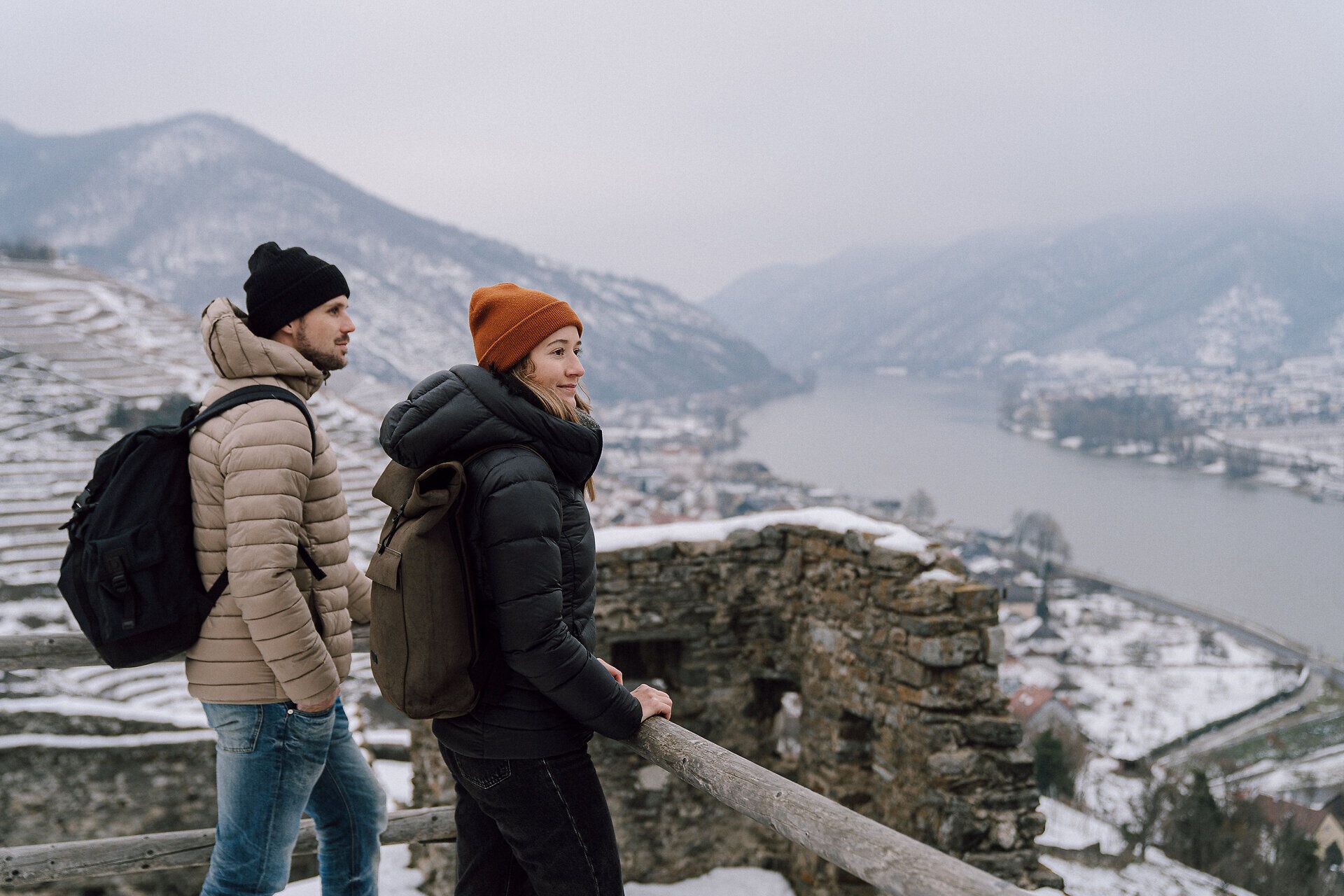 In der winterlichen Landschaft genießen zwei Wanderer die atemberaubende Aussicht auf die schneebedeckten Berge und das glitzernde Wasser des Flusses. Die frische, kalte Luft und die ruhige Atmosphäre laden dazu ein, die Schönheit der Natur in vollen Zügen zu erleben.