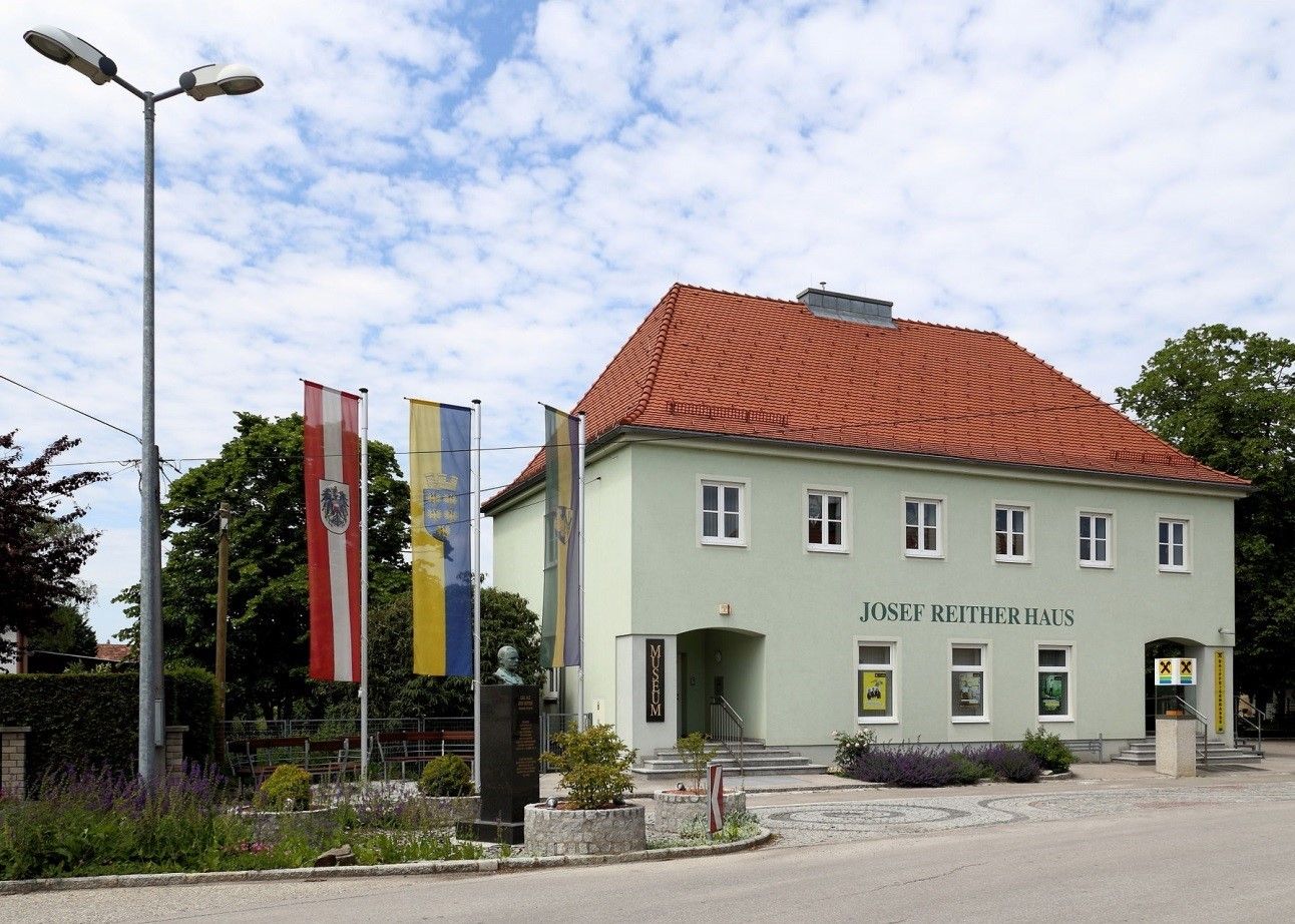 Josef Reither house with flags and bust in the foreground.