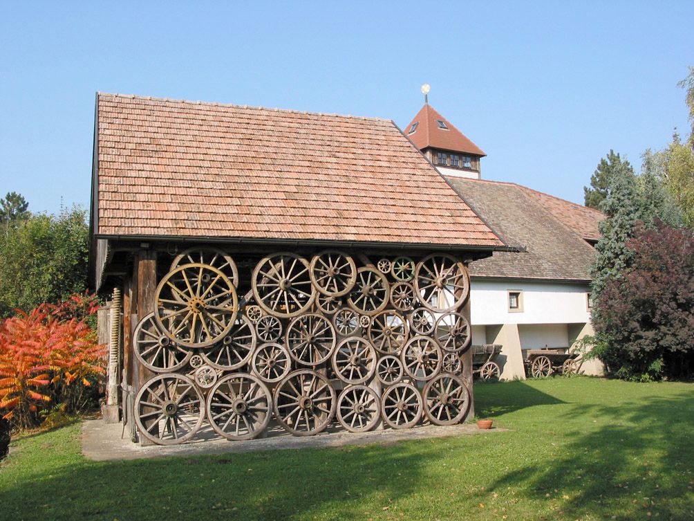 A building with a façade made of old wagon wheels, surrounded by trees and a lawn.