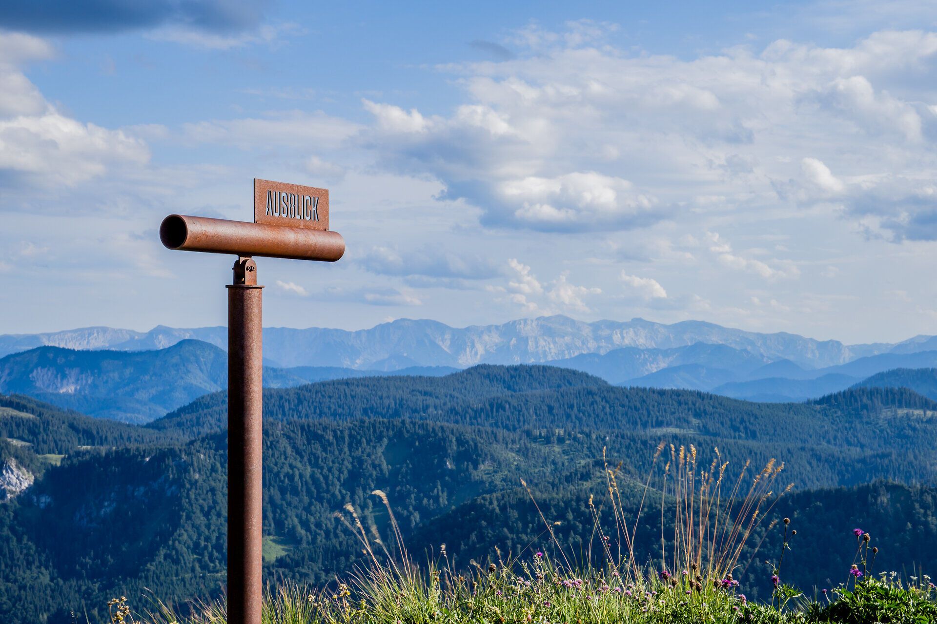 The majestic peaks of the Grosser Ötscher rise proudly against the clear sky, while the rolling hills and flowering meadows provide an inviting backdrop for hikers. A telescope invites you to enjoy the breathtaking view and experience the beauty of nature to the full.