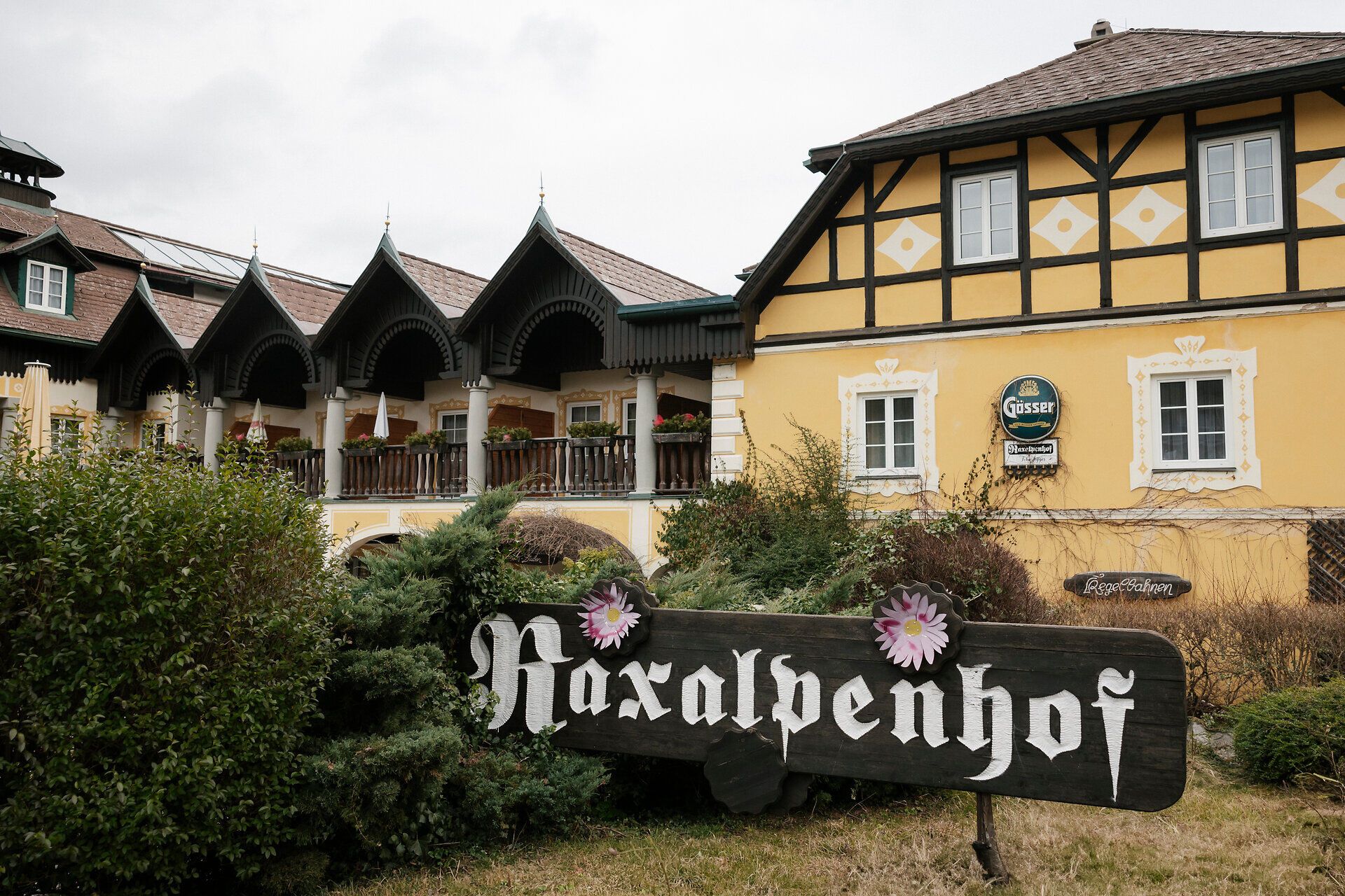 Traditional inn with a yellow façade and wooden verandas, in front of which is a sign reading "Raxalpenhof".