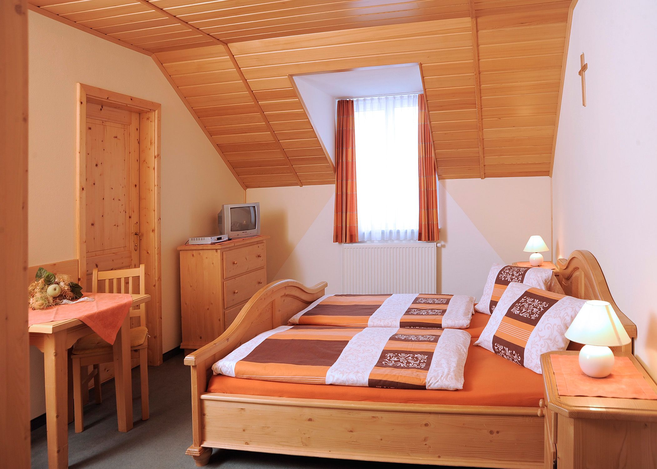 Cozy guest room with wooden furniture, double bed, small table, TV and sloping ceiling.