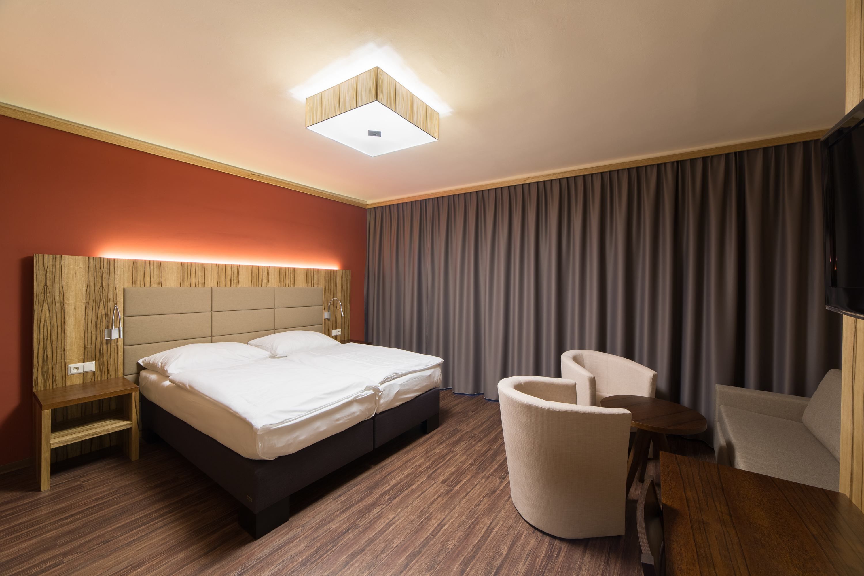 Modern hotel room with double bed, wooden furniture and curtains.