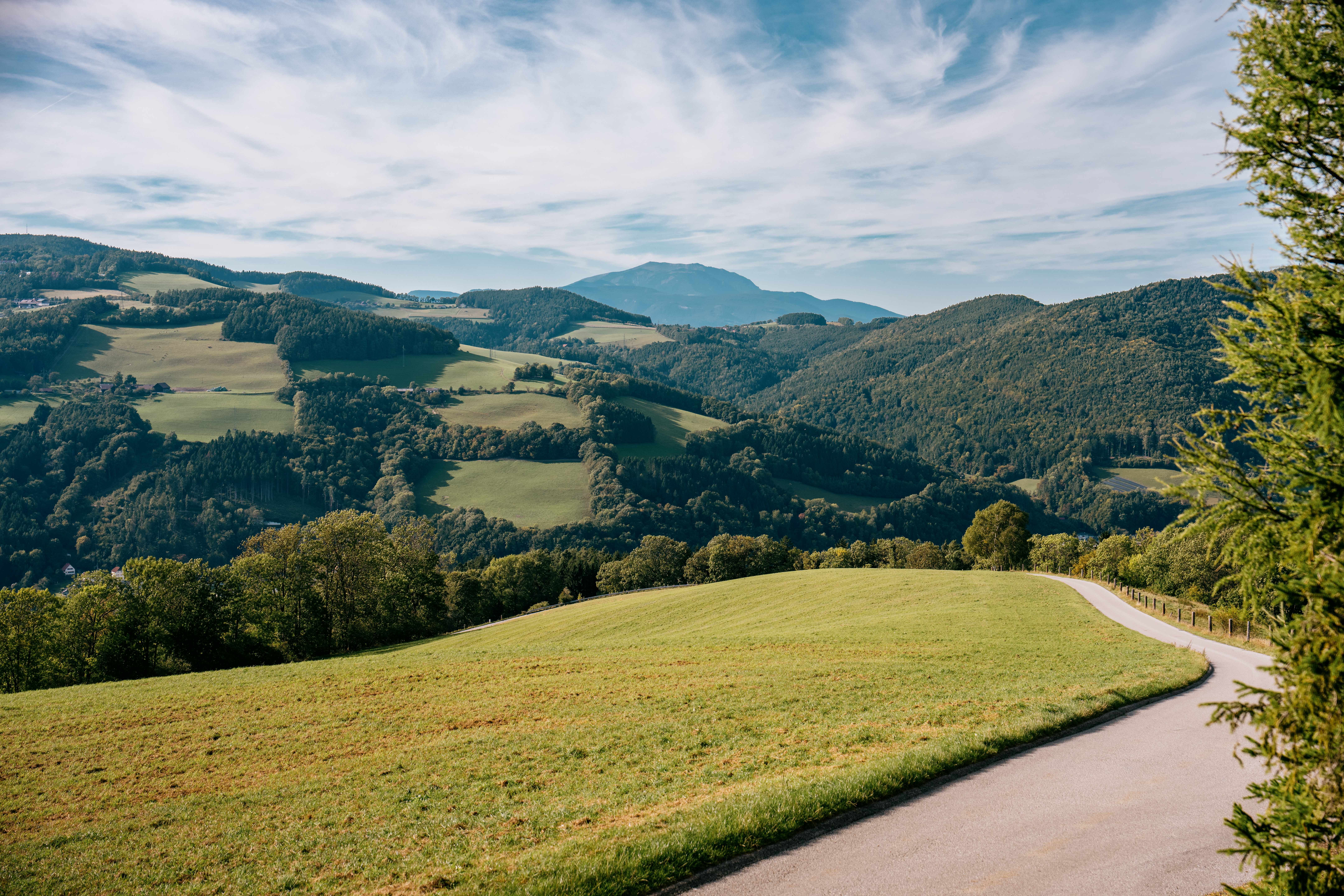 Panoramic view of a hilly landscape with green meadows and wooded hills under a blue sky.
