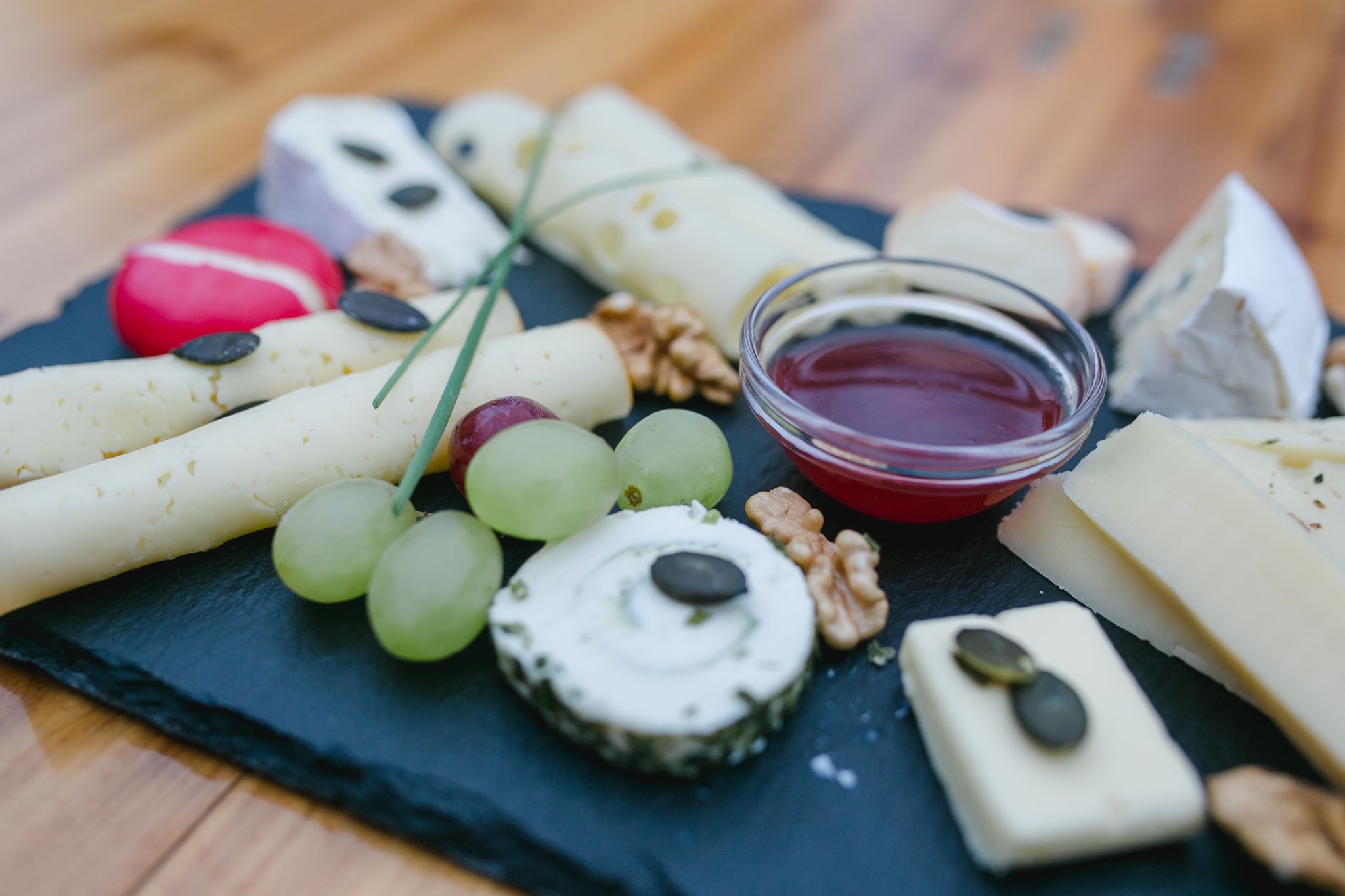 Cheese platter with grapes, nuts and dip on a slate plate.