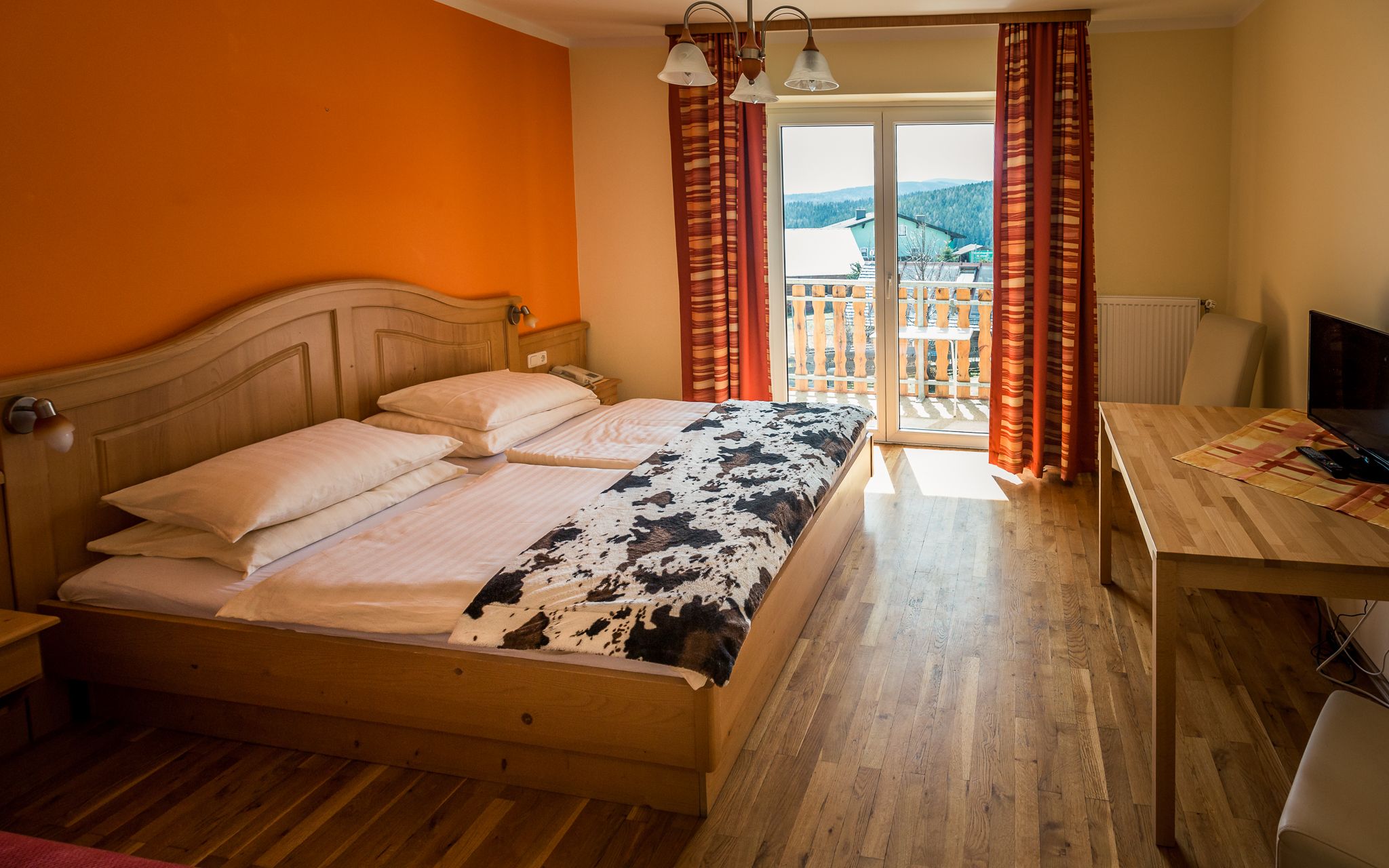 Comfortable hotel room with double bed, wooden furniture and balcony with a view.
