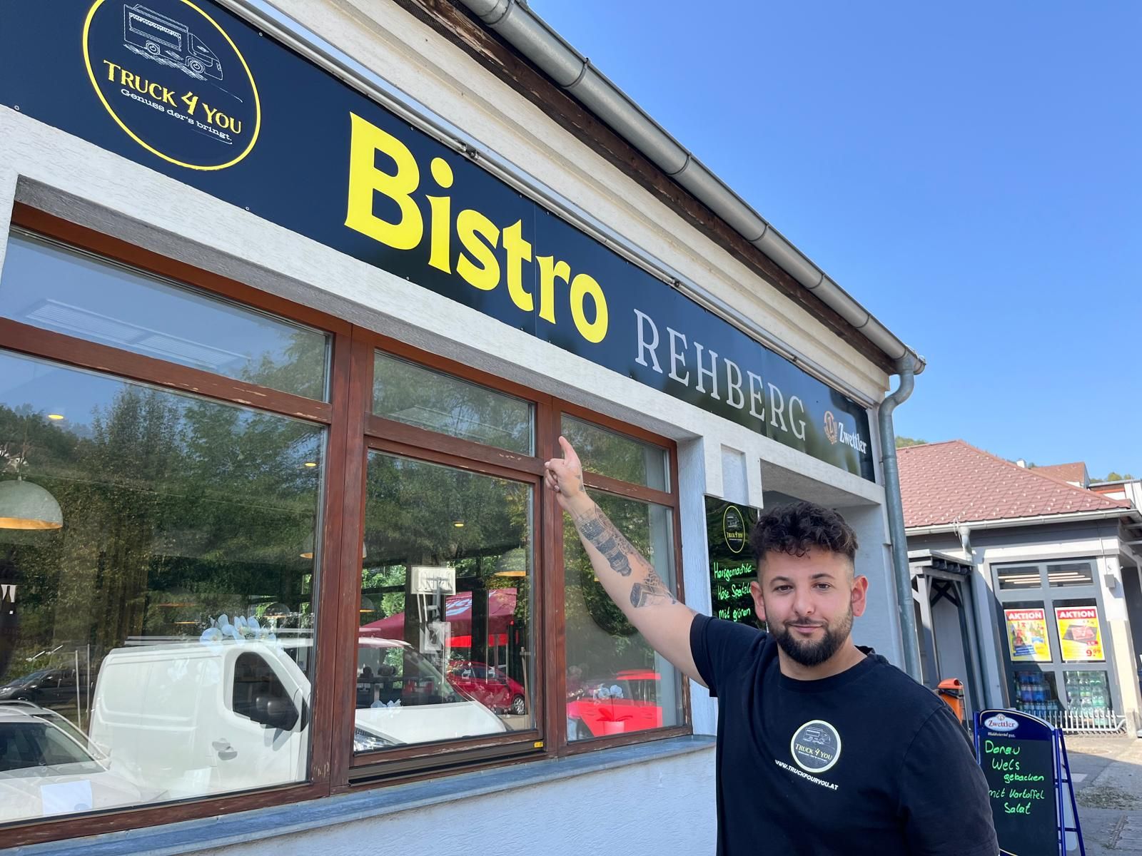 A man points to a sign saying 'Bistro Rehberg'.
