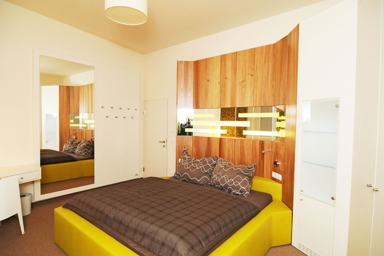 Modern furnished bedroom with yellow bed and wood paneling on the wall.