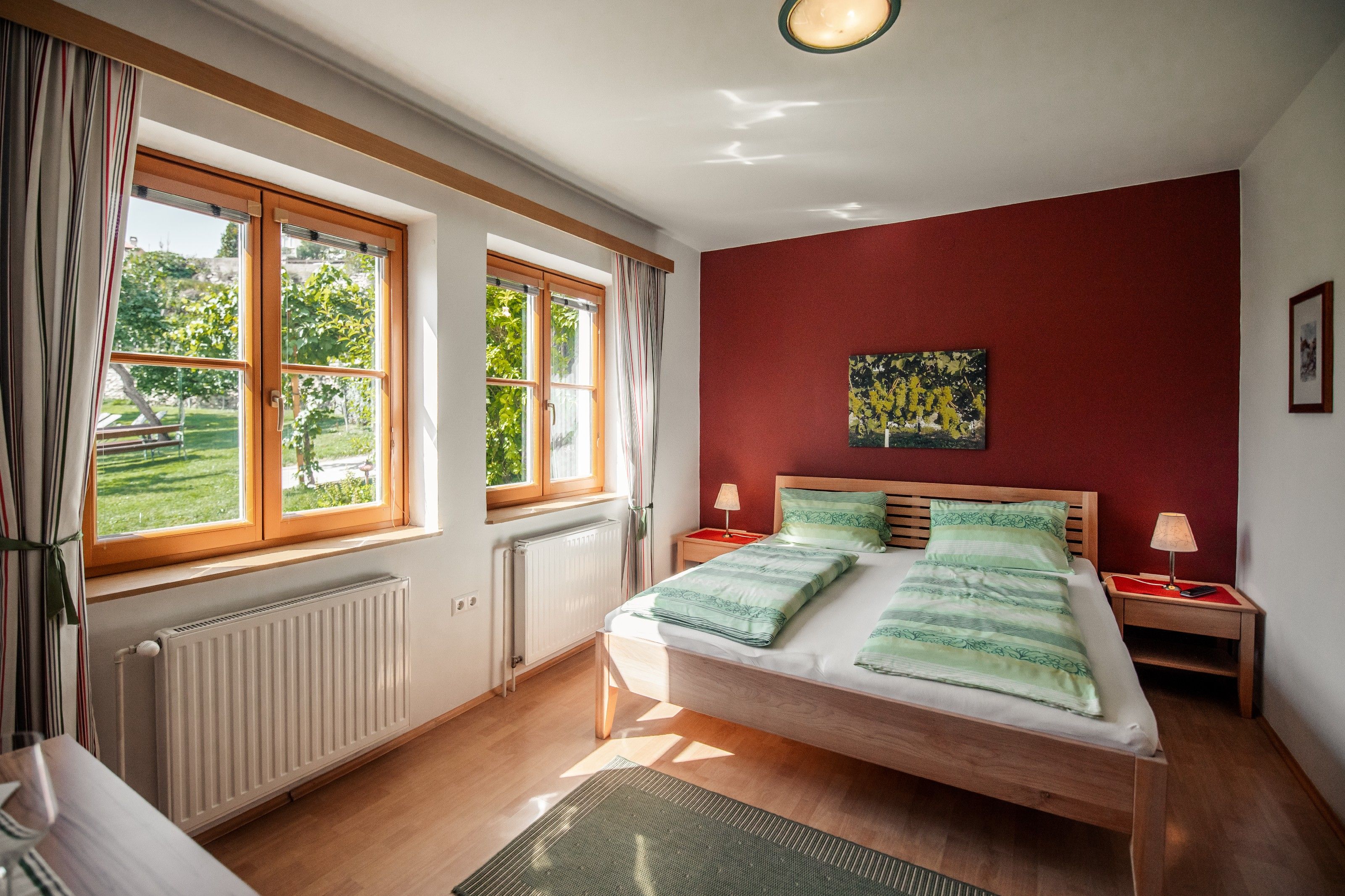 Bright bedroom with double bed, red walls and large windows with a view of the greenery.