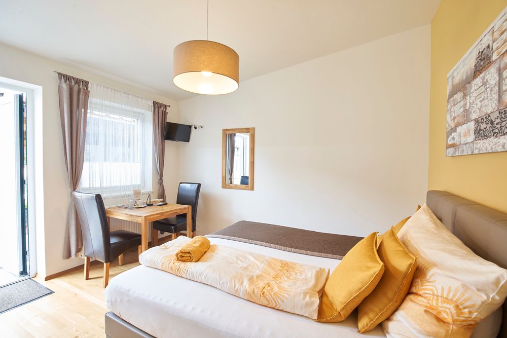 Bright guest room with bed, table, chairs and TV.