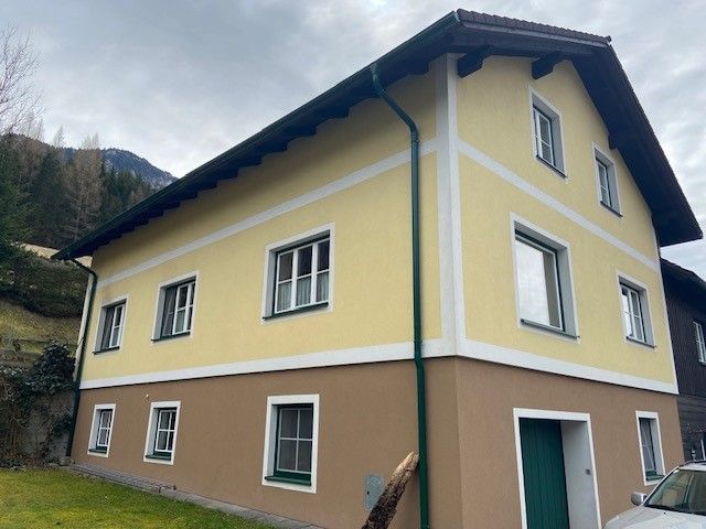 Two-storey yellow-brown house with white window frames and green downpipes.