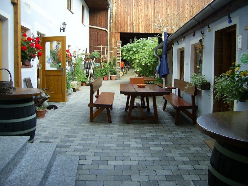 Inner courtyard of a farm with wooden tables and benches, surrounded by plants and flowers.