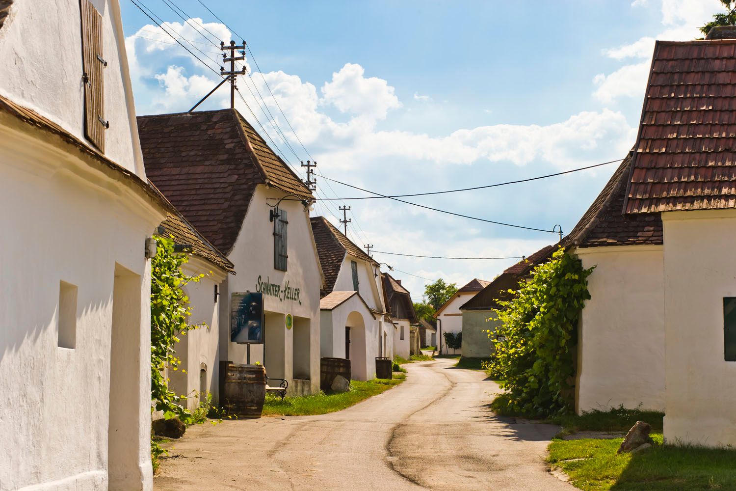 A picturesque wine cellar lane with white buildings and tiled roofs under a blue sky.