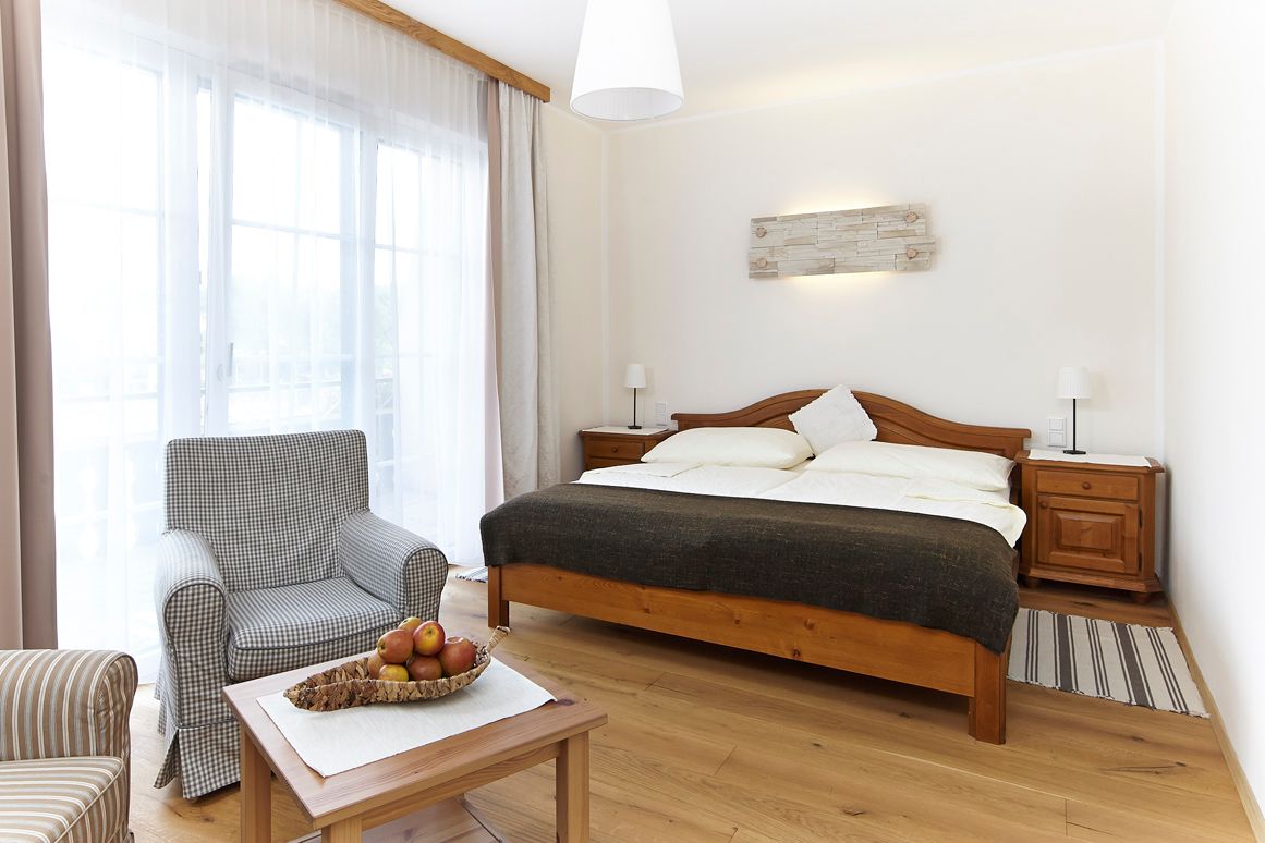 Bright room with double bed, armchair and table with fruit bowl.