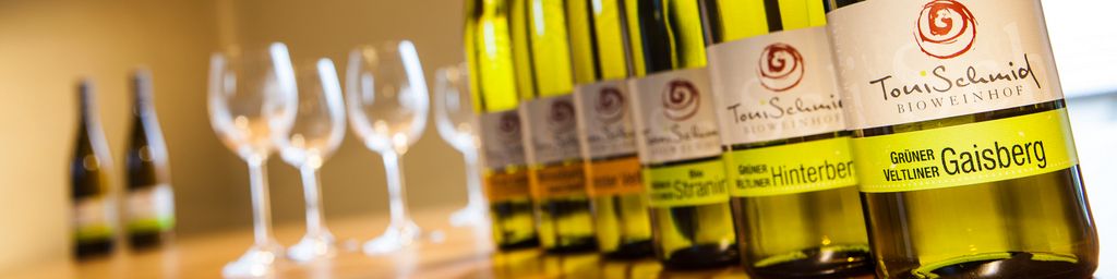 Row of wine bottles with glasses in the background.