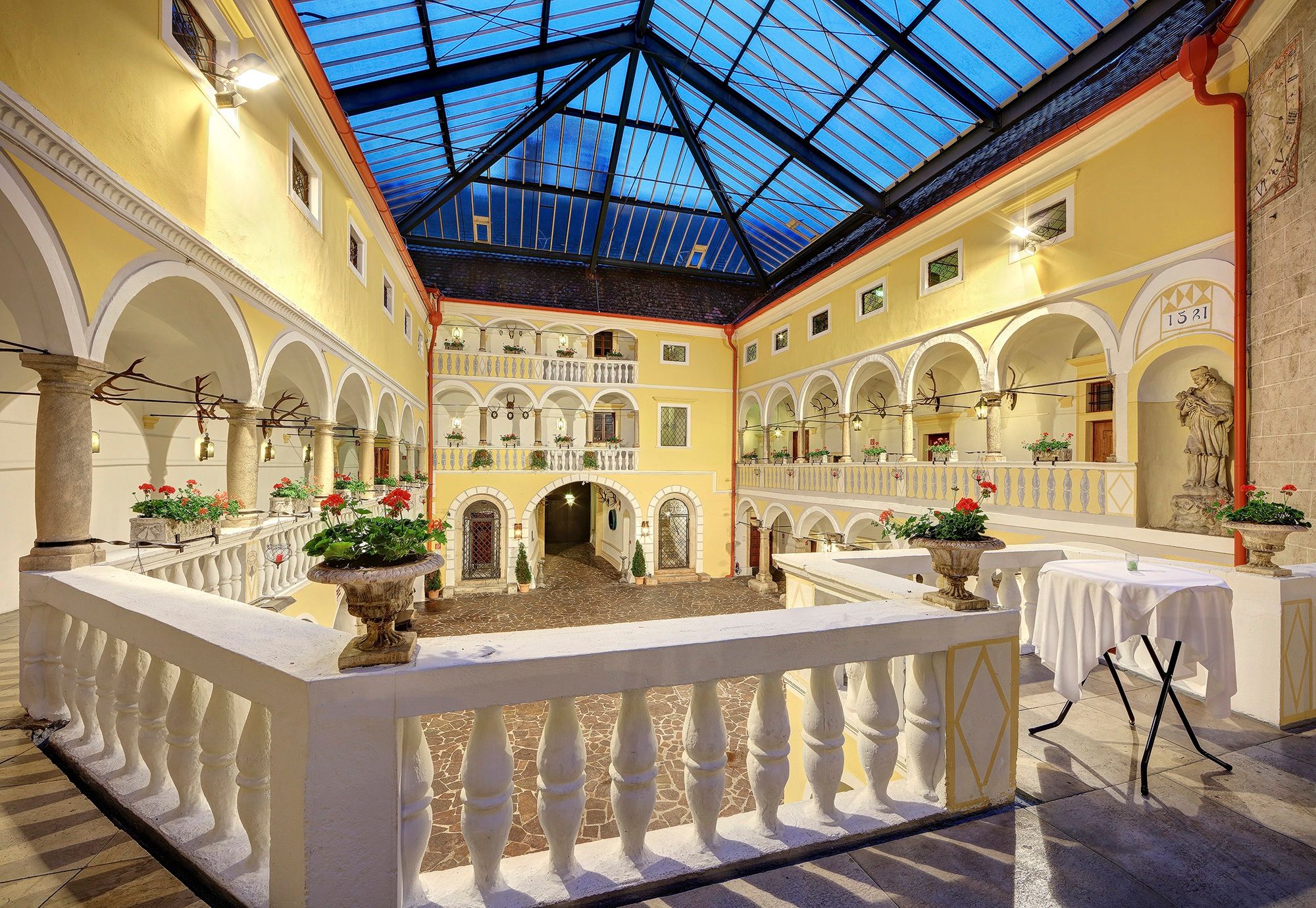 Courtyard with arcades, yellow facades, a glass roof, and floral arrangements at H_WeikersdorfArkadenh_web.