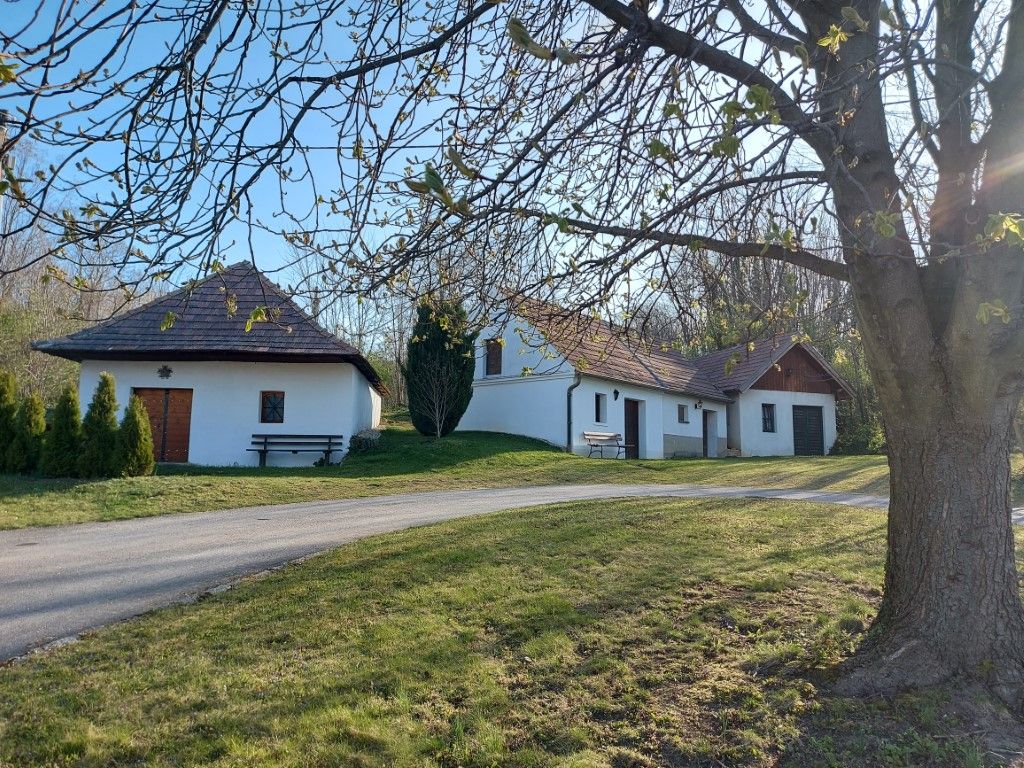 White buildings with red roofs in a rural setting, trees in the foreground.