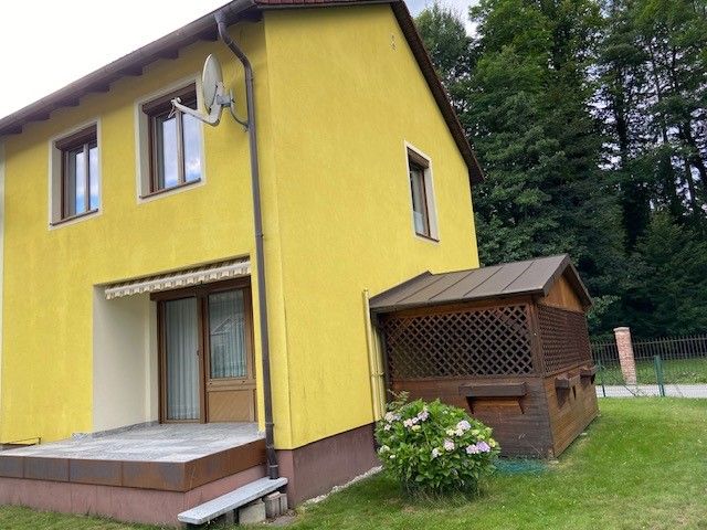 Yellow vacation home with terrace and small annex surrounded by trees.
