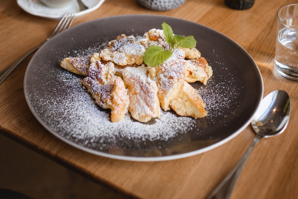 A plate of Rahmschmarrn, sprinkled with powdered sugar and garnished with mint leaves, on a wooden table.