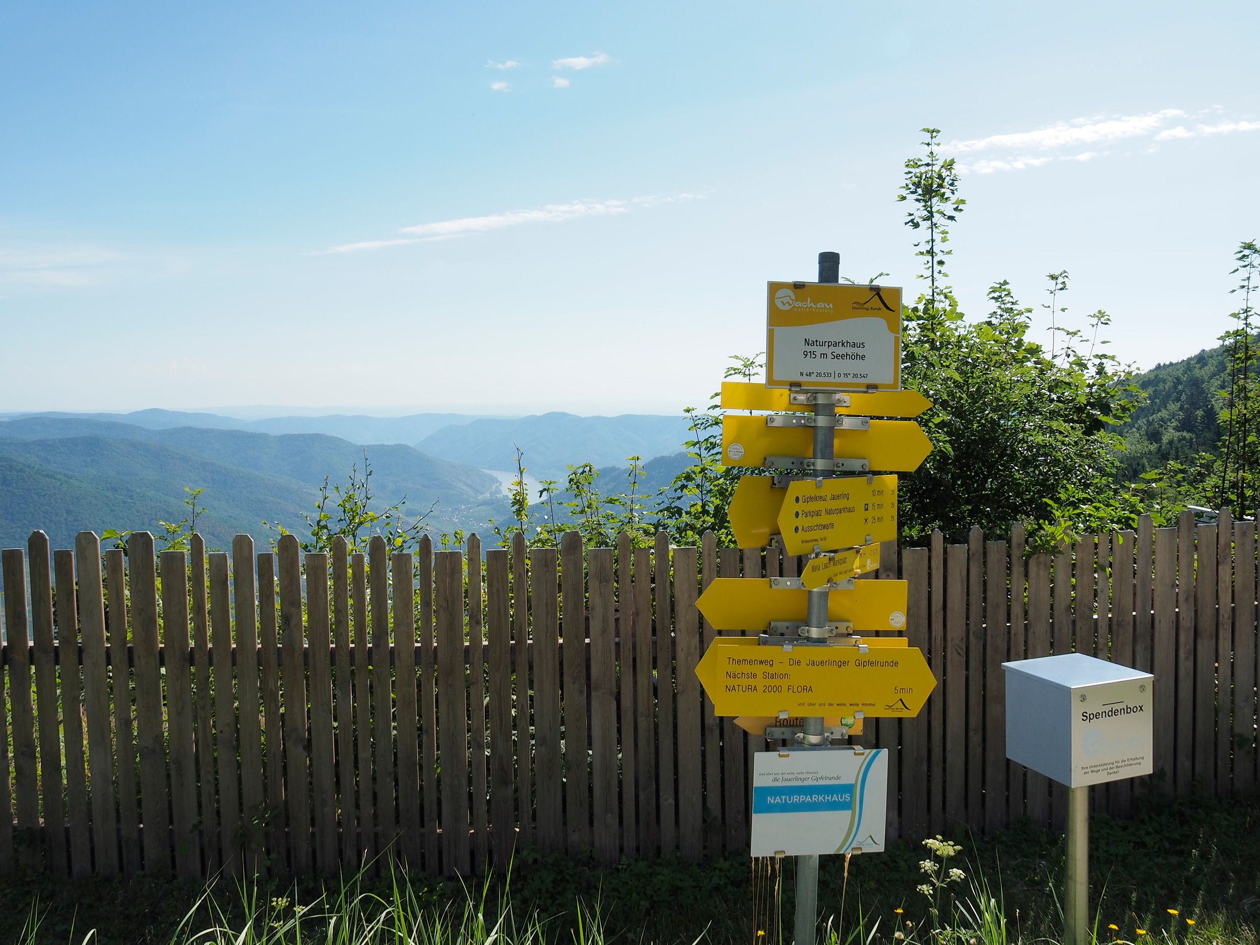 Signpost on the Jauerling with a view of wooded hills and blue sky.