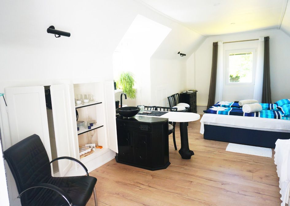 Interior view of a bright vacation home with bed, table, chairs and kitchenette.