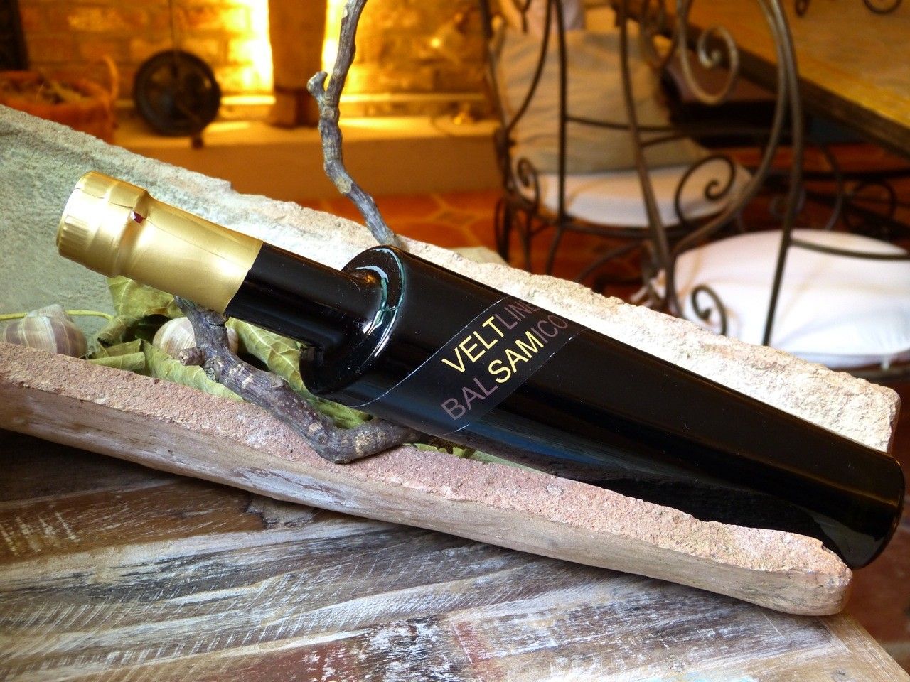 A black vinegar bottle with a golden cap lies in a rustic wooden bowl.