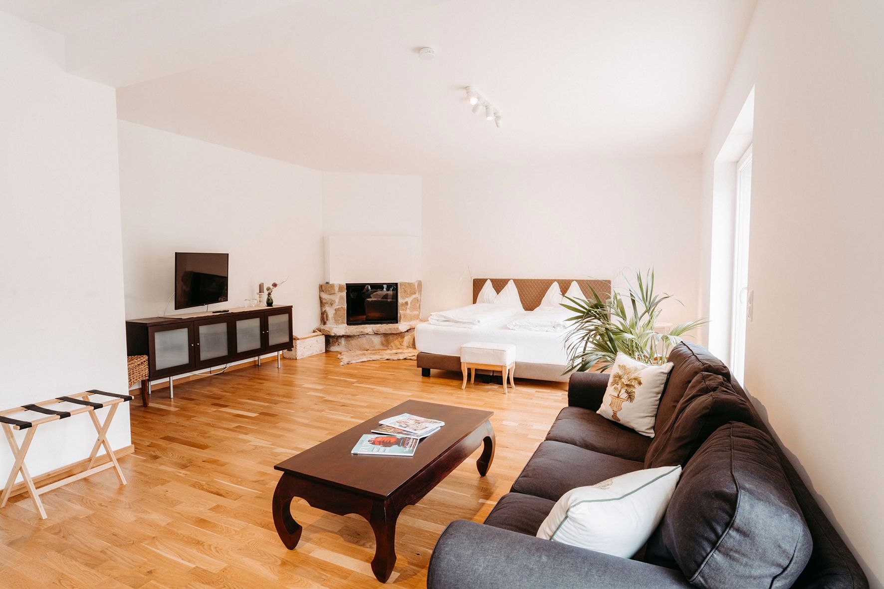 Bright room with sofa, coffee table, TV, fireplace and double bed.