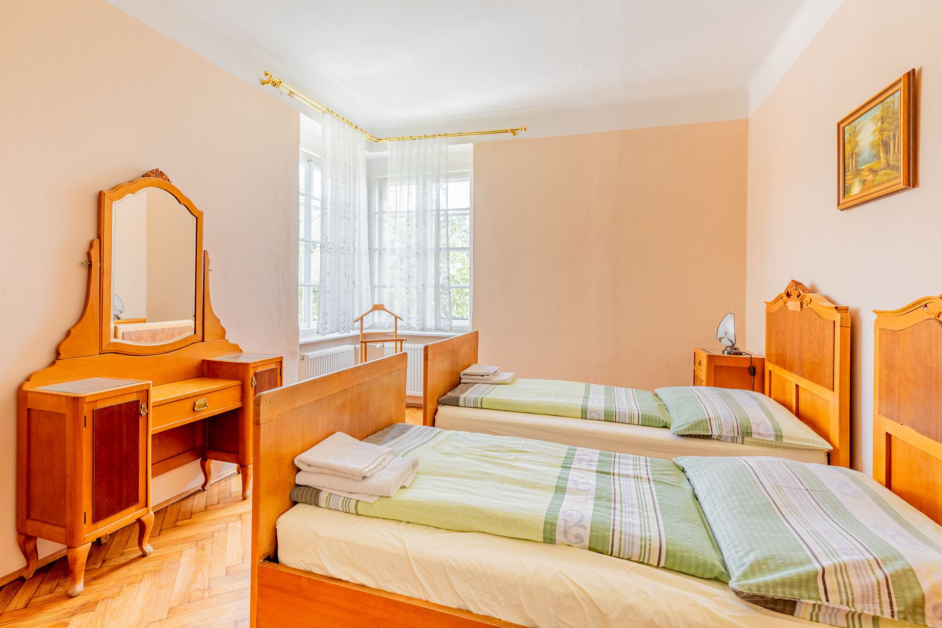 A traditional bedroom with two single beds, a dressing table with mirror and a window with white curtains.