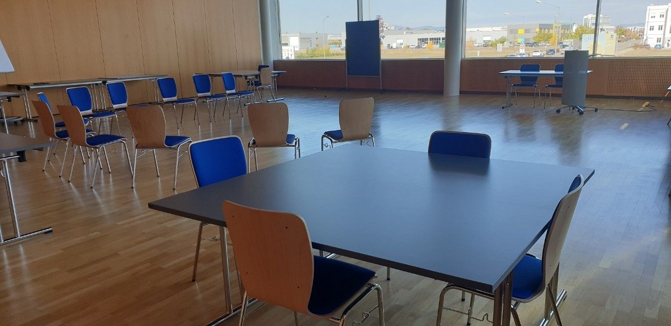 An empty seminar room with tables and chairs, a wooden floor and large windows.