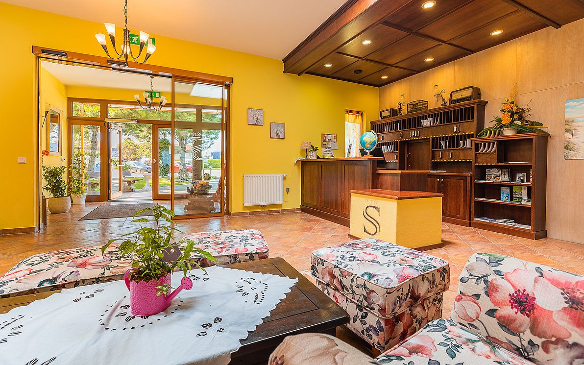 Hotel reception with yellow walls, wooden furniture and floral pattern armchairs.