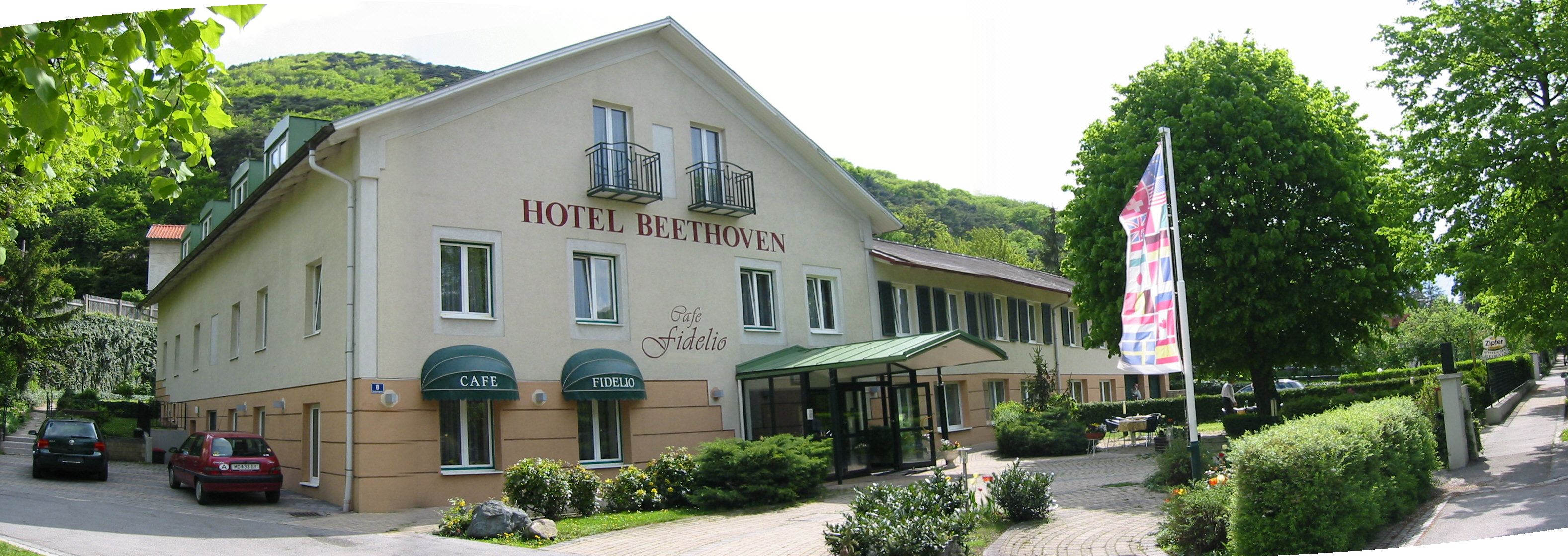 Exterior view of the Hotel Beethoven with Café Fidelio, surrounded by trees and flags.