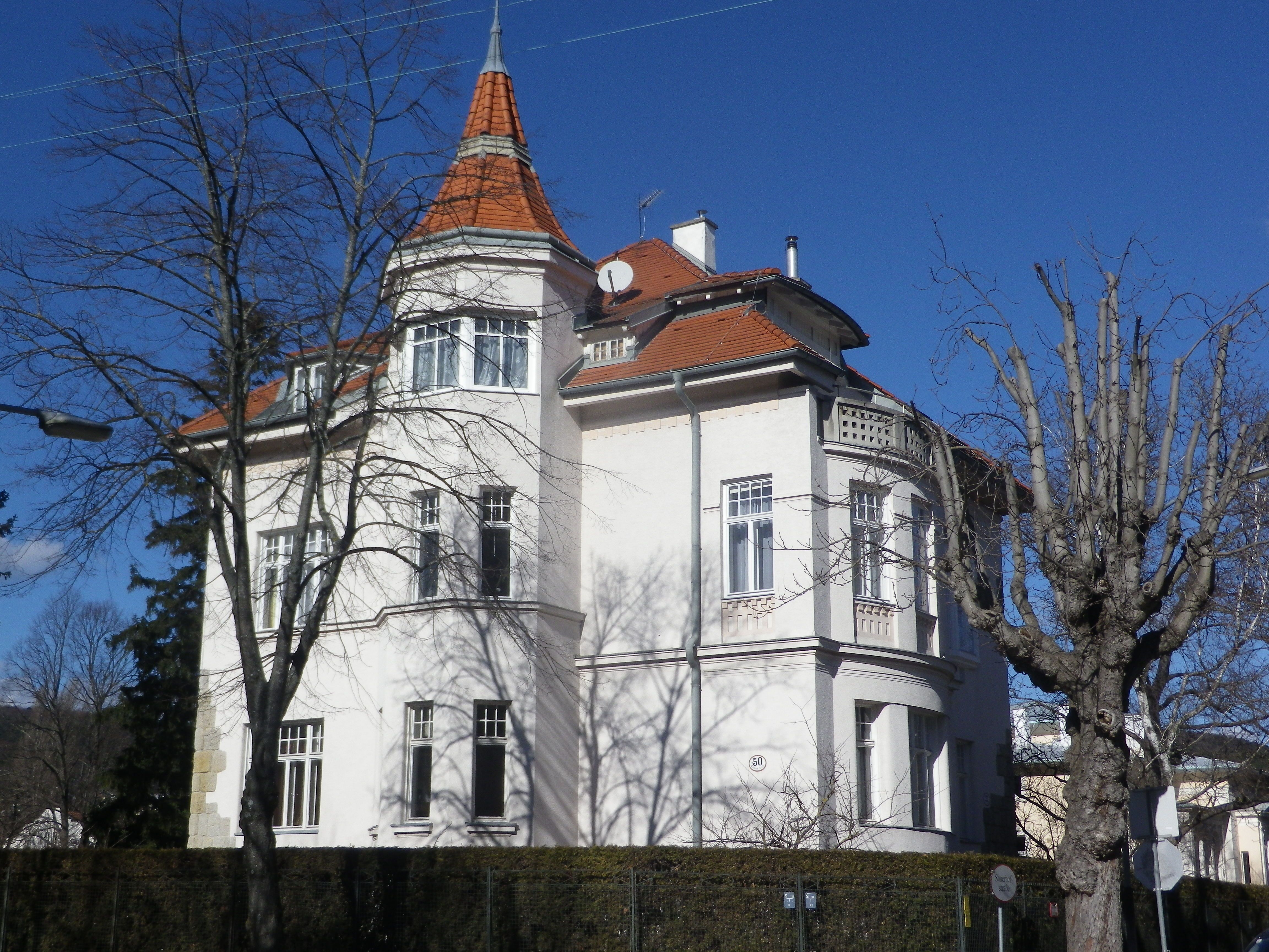 Large white house with a red roof and tower, surrounded by bare trees.