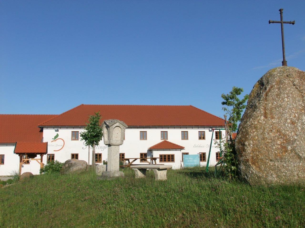 A farm with a red roof and a large stone with a cross in the foreground.