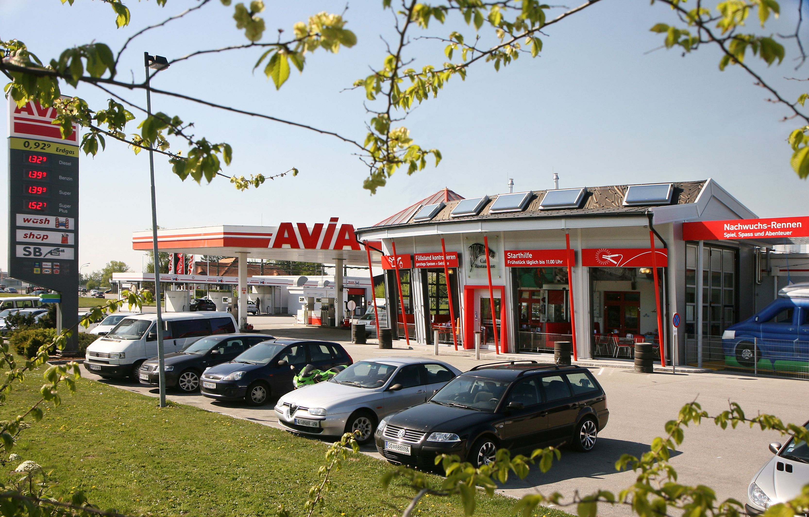 Petrol station with AVIA logo and several parked cars in the foreground.