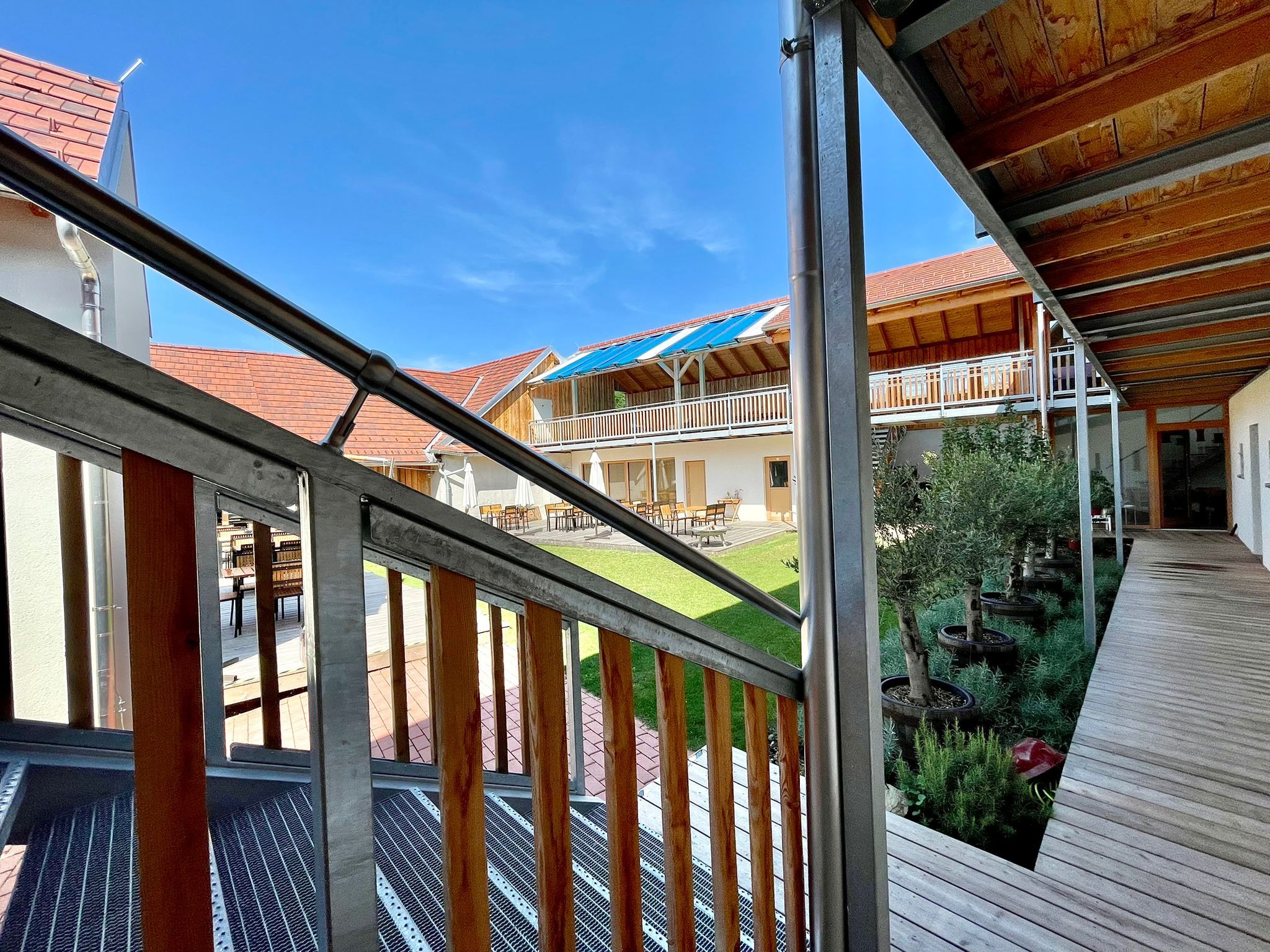 Inner courtyard with wooden veranda and plants, surrounded by buildings with red roofs.