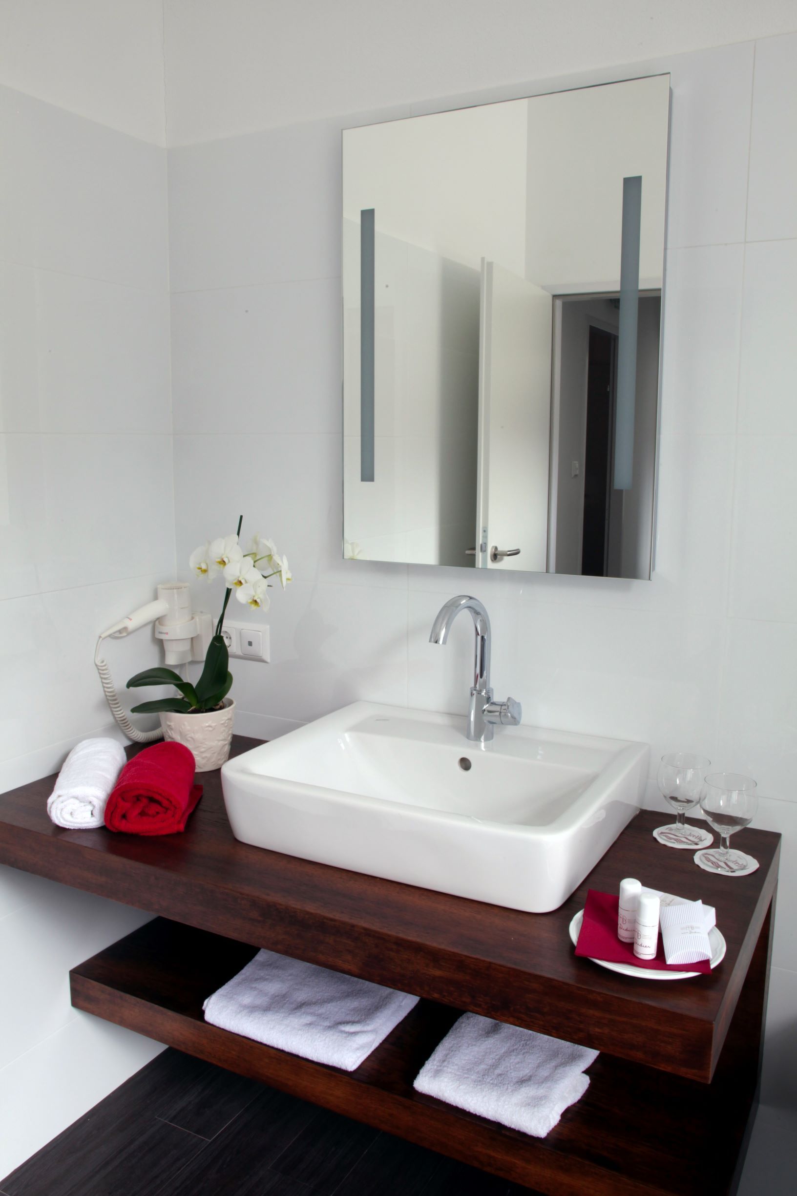 Modern bathroom with washbasin, mirror, towels and orchid.